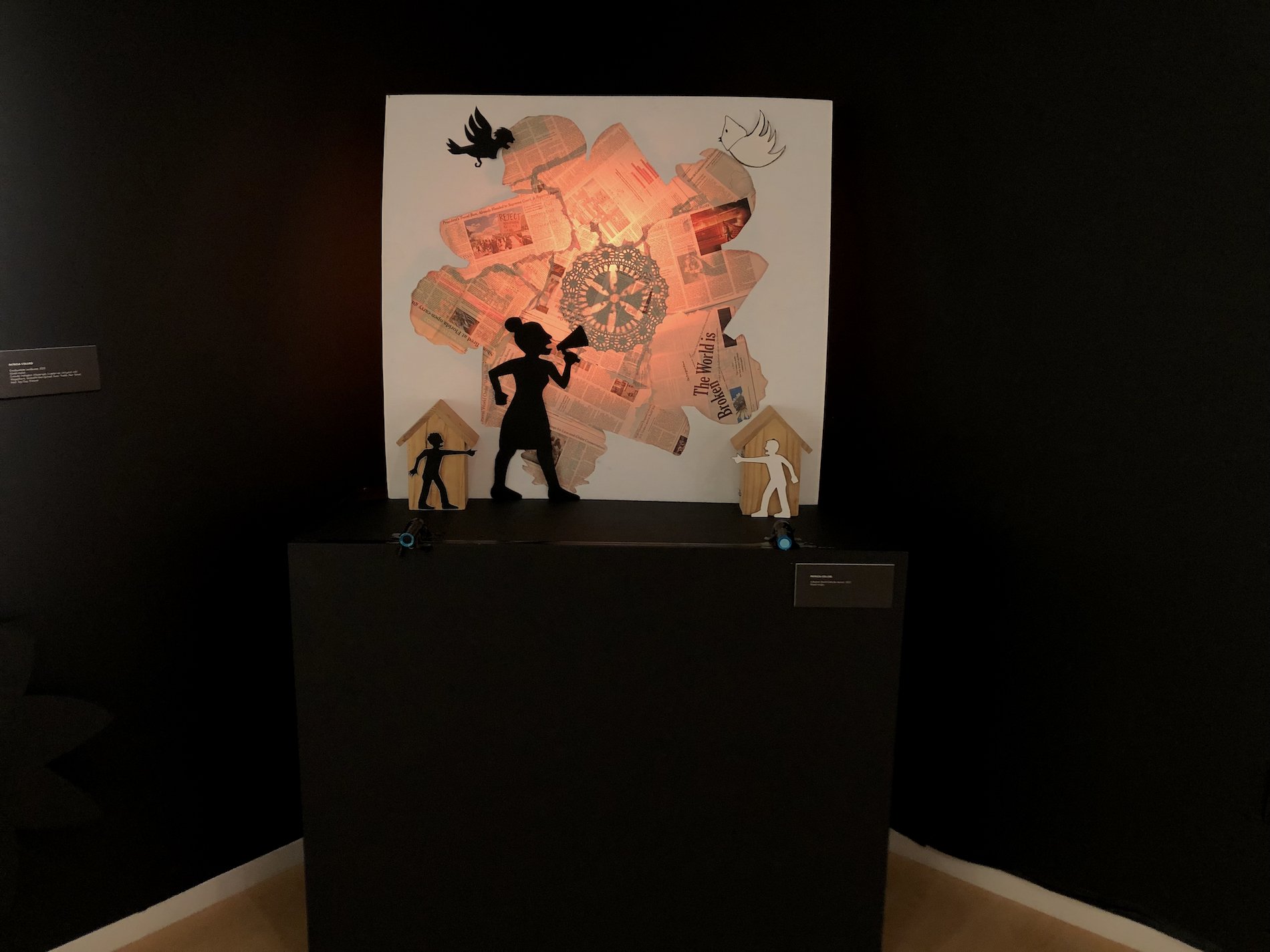 Broken World Calls for Action" mixed media installation with back lighting, flashlights, corrugated plastic wood, newspaper collage, paper cuts, thread.
