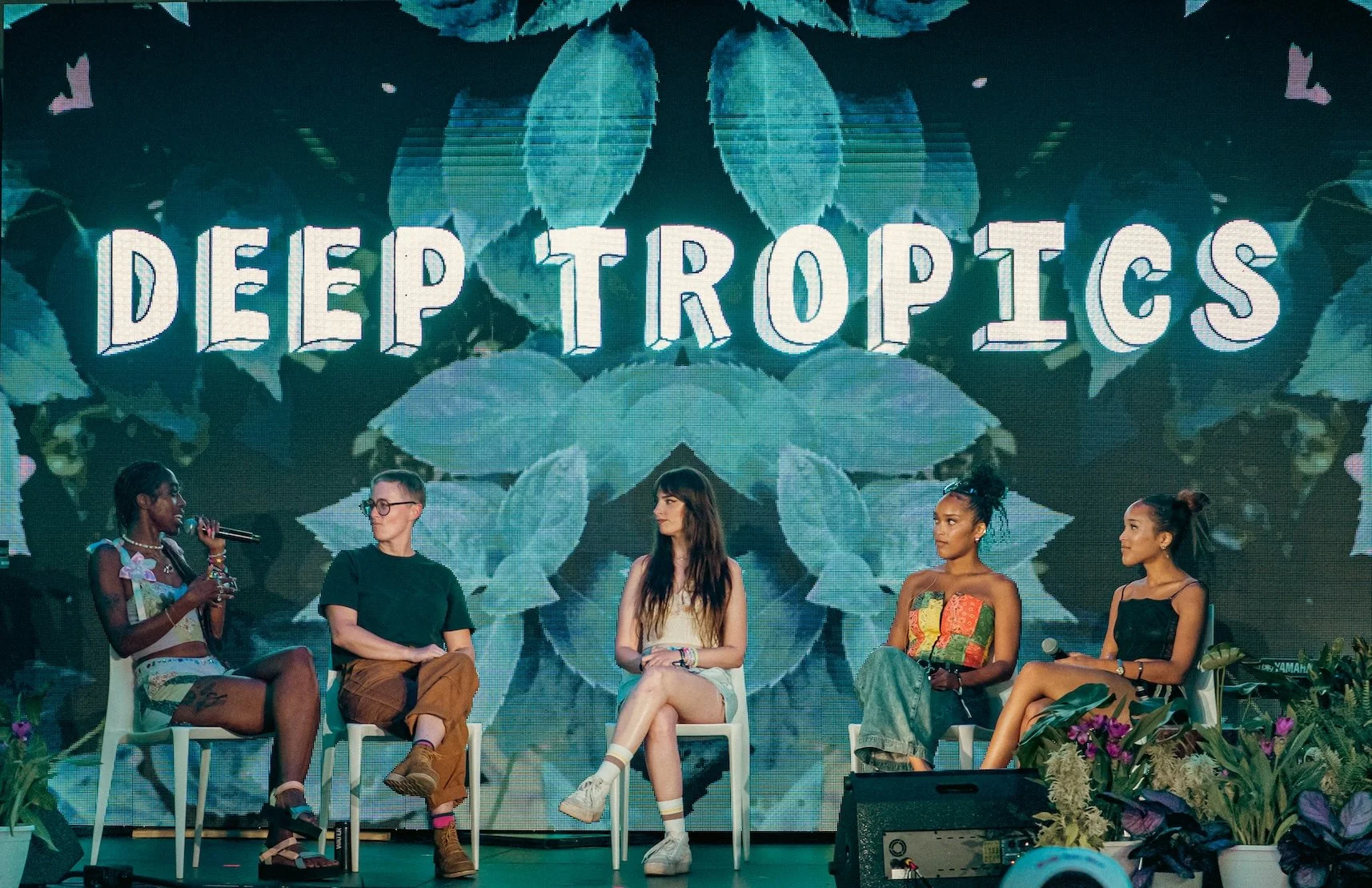 Four people sit on stage in front of a colorful DEEP TROPICS sign, having a panel discussion.