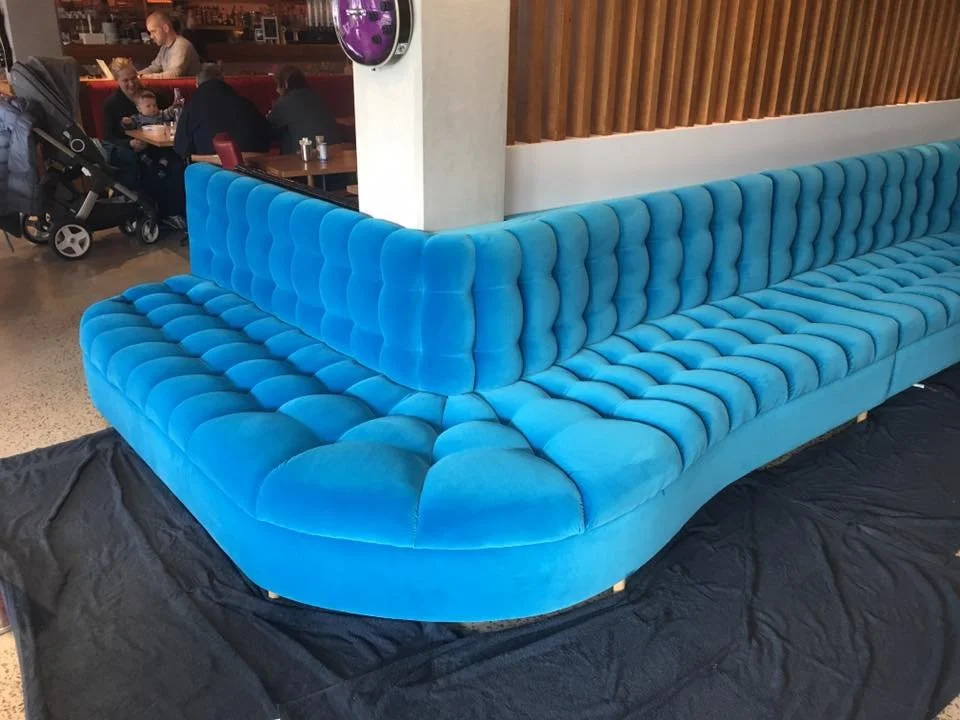 A large, bright blue, tufted sectional sofa with curved edges in a modern restaurant or bar setting.