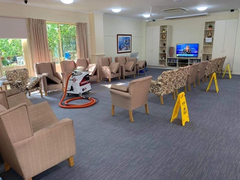Empty waiting room with chairs, a television, and cleaning equipment set up, indicating cleaning or maintenance in progress.