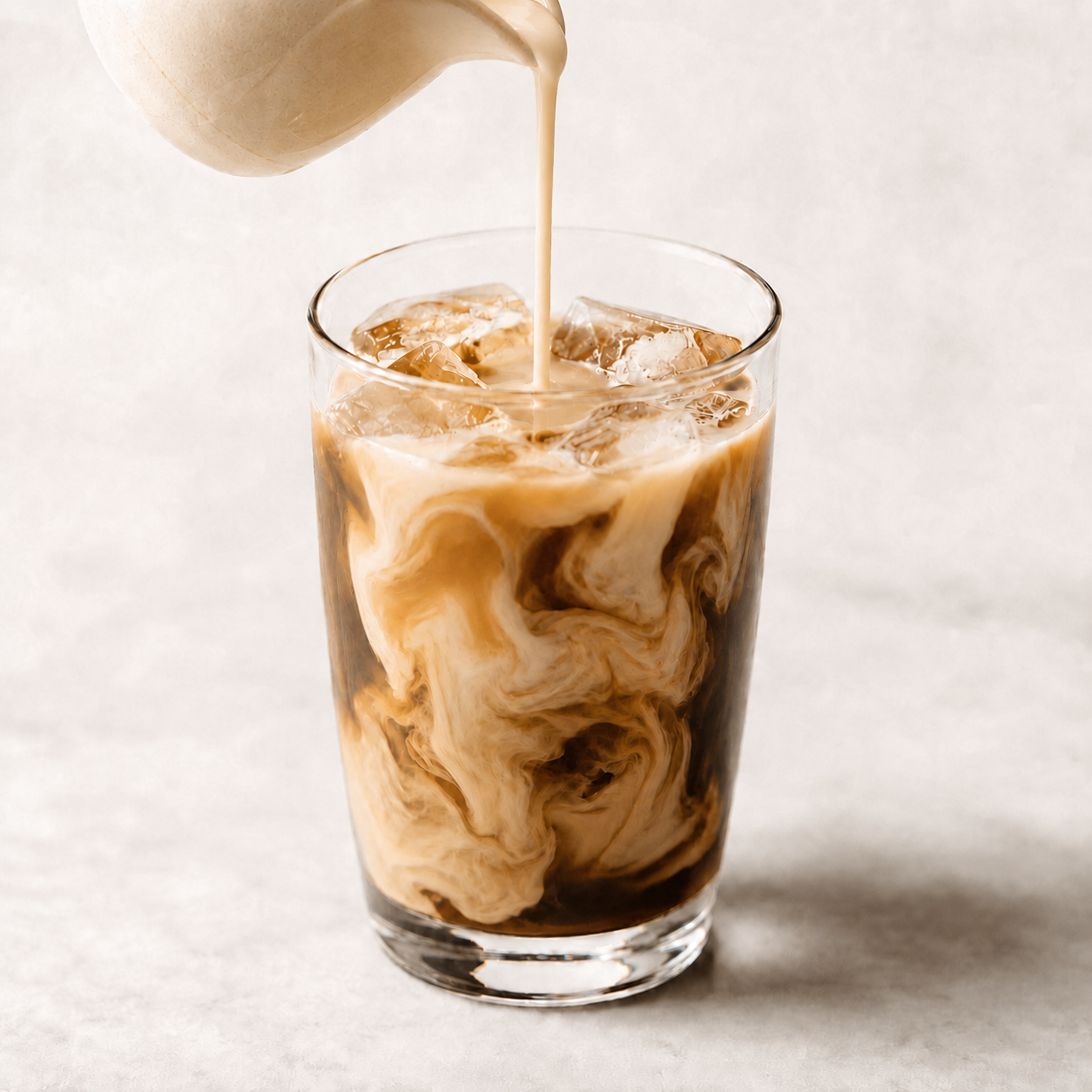 Vör Cashew Nut Milk Base poured into iced coffee, creating smooth creamy swirls through the cold brew.