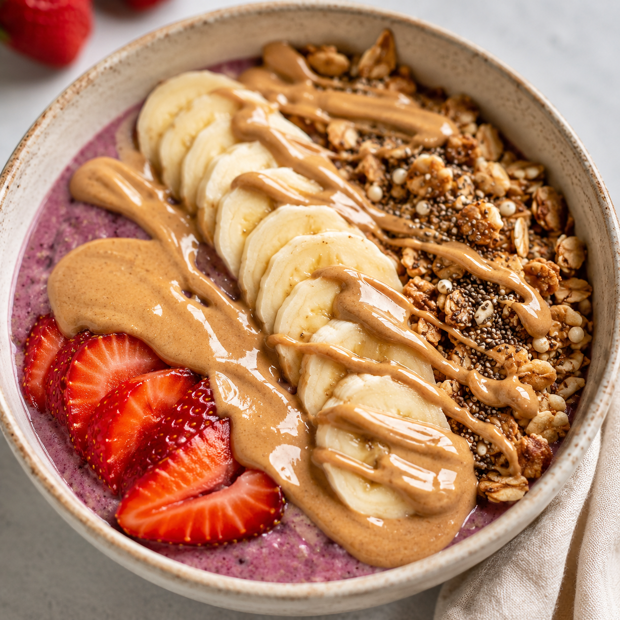 Vör almond butter drizzled over a berry smoothie bowl with banana, strawberries, granola, and chia seeds.