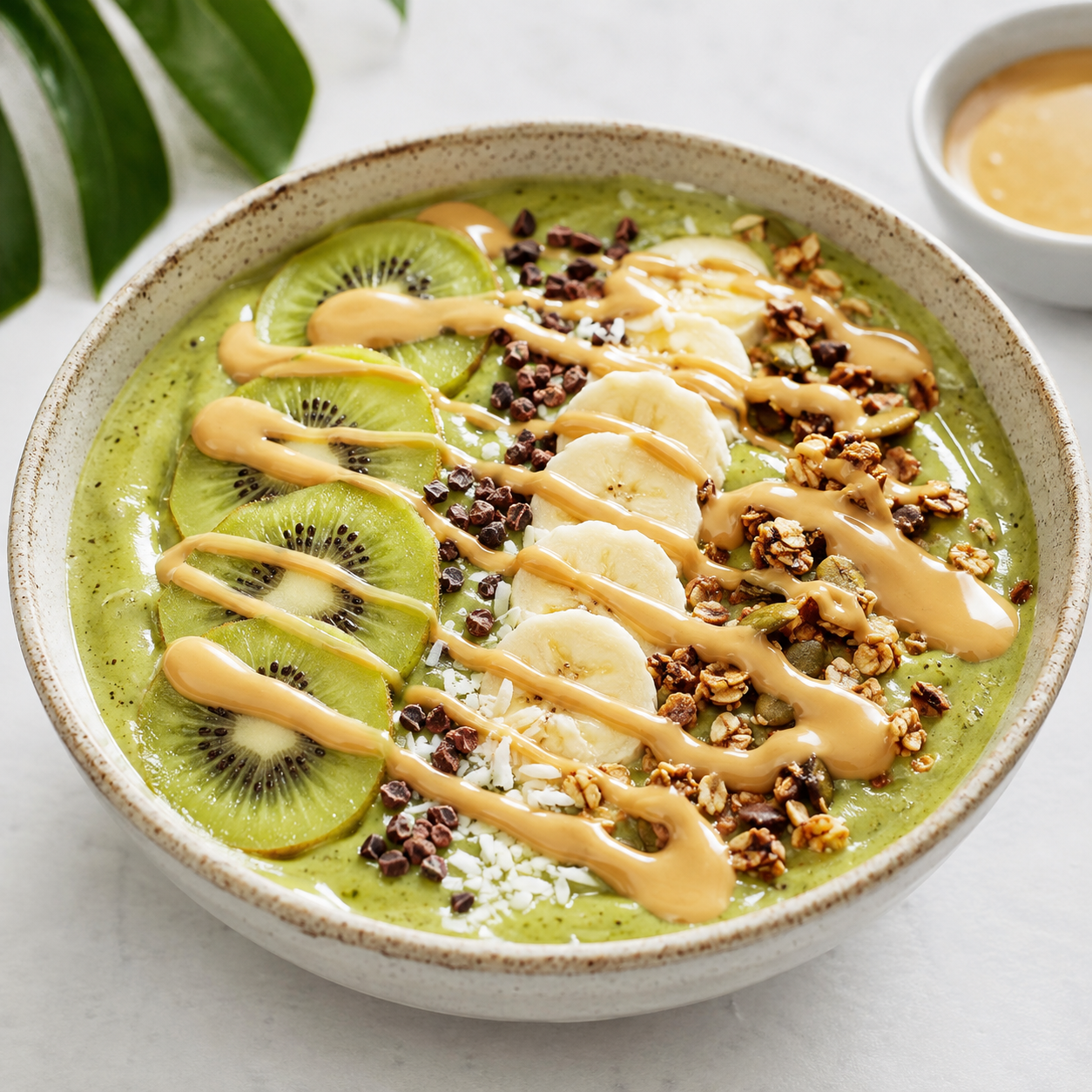 Green smoothie bowl topped with kiwi, banana, granola, cacao nibs, coconut, and Vör Peanut Drizzle.