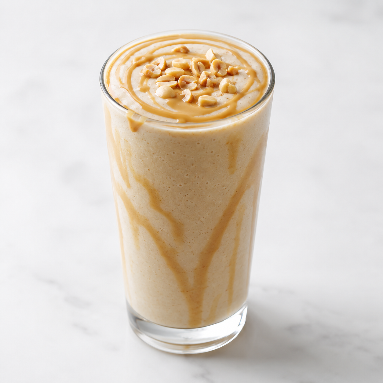 Creamy peanut smoothie in a clear glass topped with chopped peanuts and Vör Peanut Drizzle.