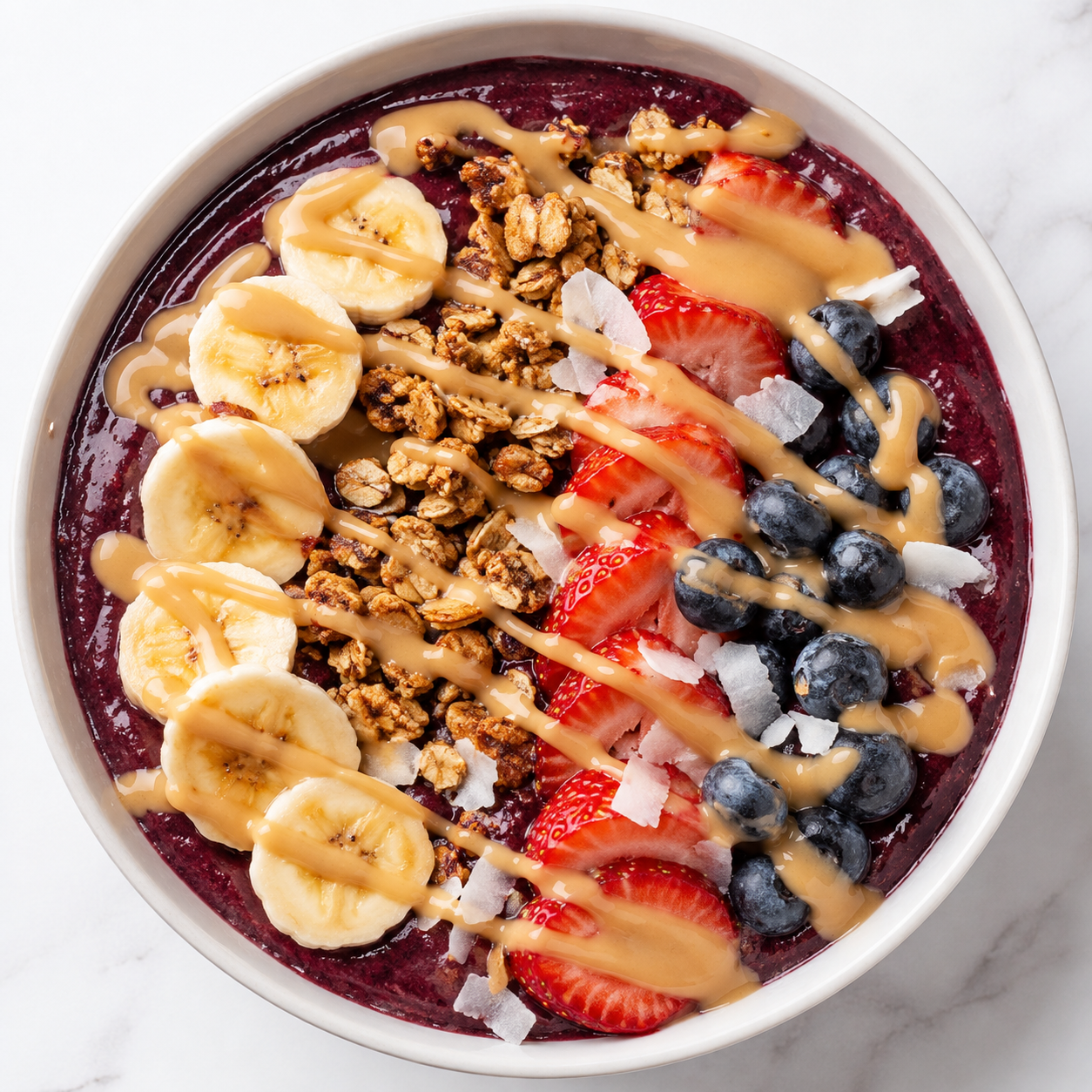 Berry acai smoothie bowl with banana, strawberries, blueberries, granola, coconut, and Vör Peanut Drizzle.