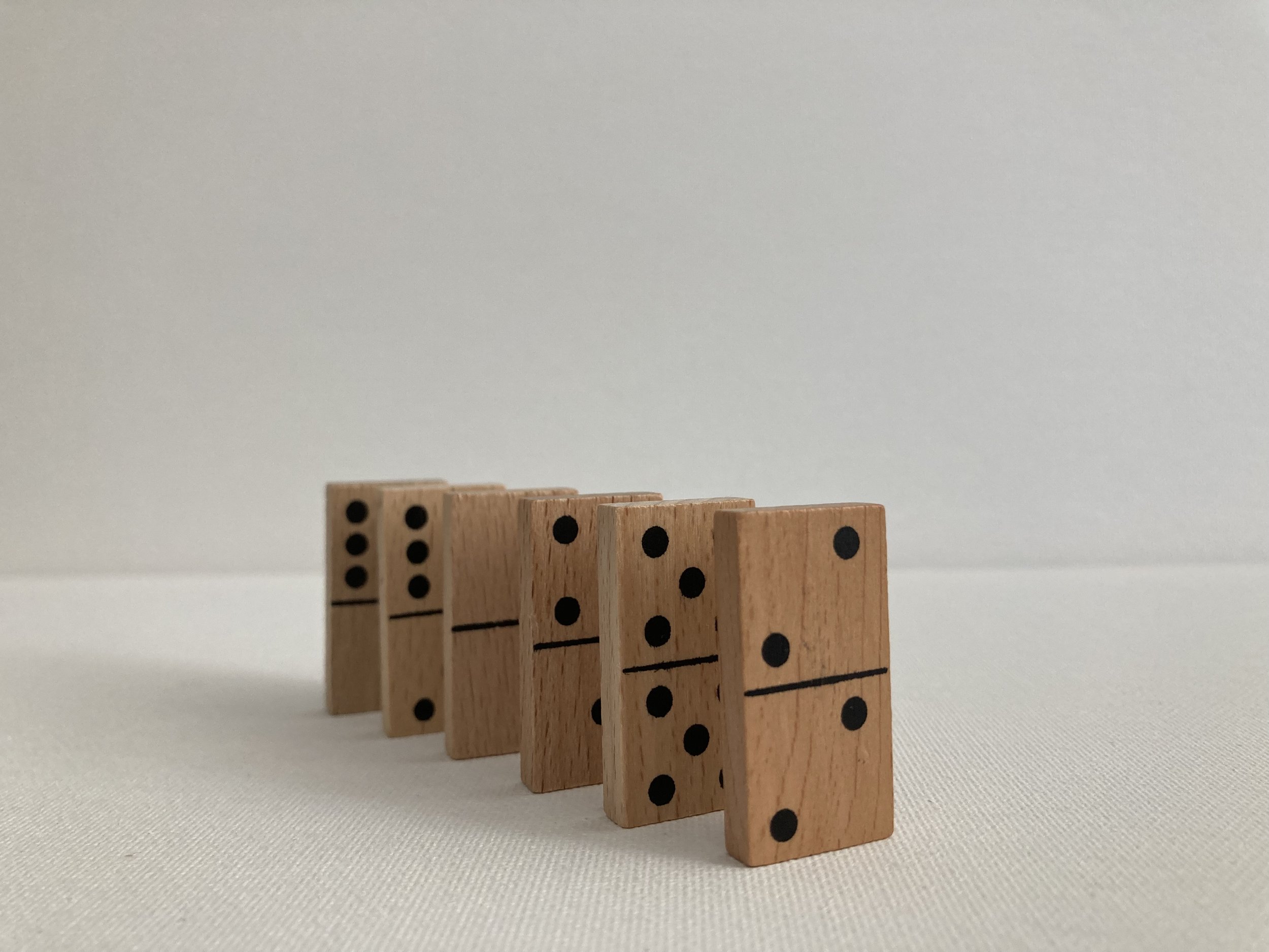 A line of six wooden dominoes with black pips, standing on a white surface against a plain white background, arranged in order from one to six.