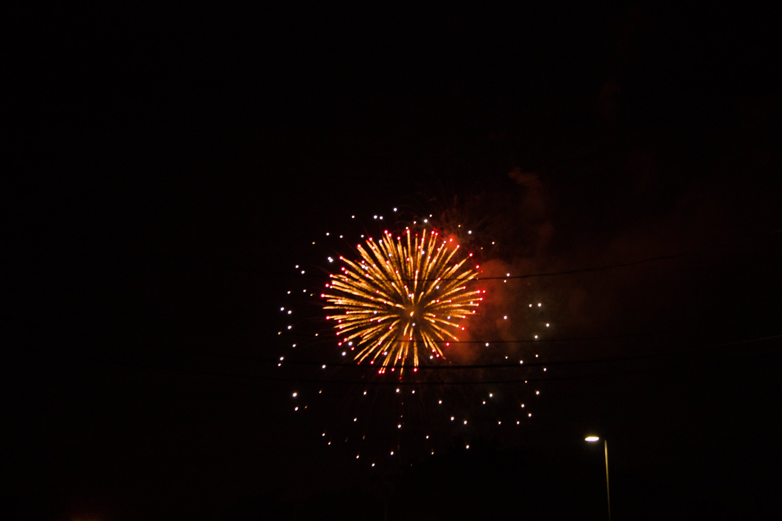 Bright fireworks exploding in the night sky with a lamppost visible in the lower right.