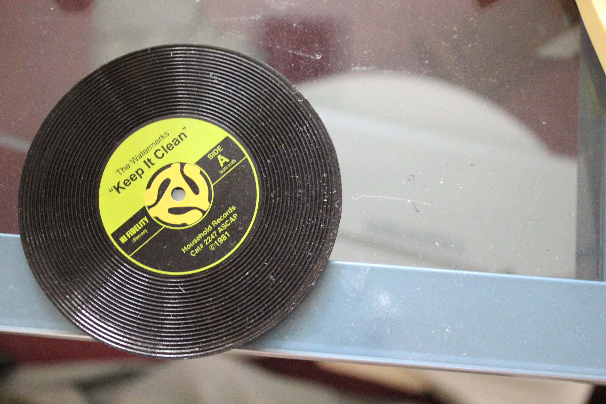 A vintage black vinyl record with a yellow label, titled 'Keep It Clean', resting on a glass surface.