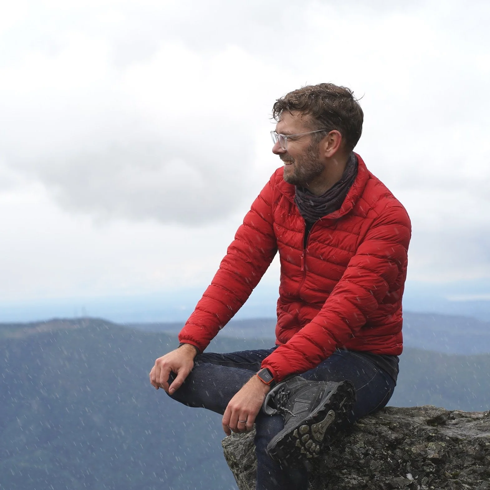 Andrew sitting on a rock looking left with a distant horizon behind.