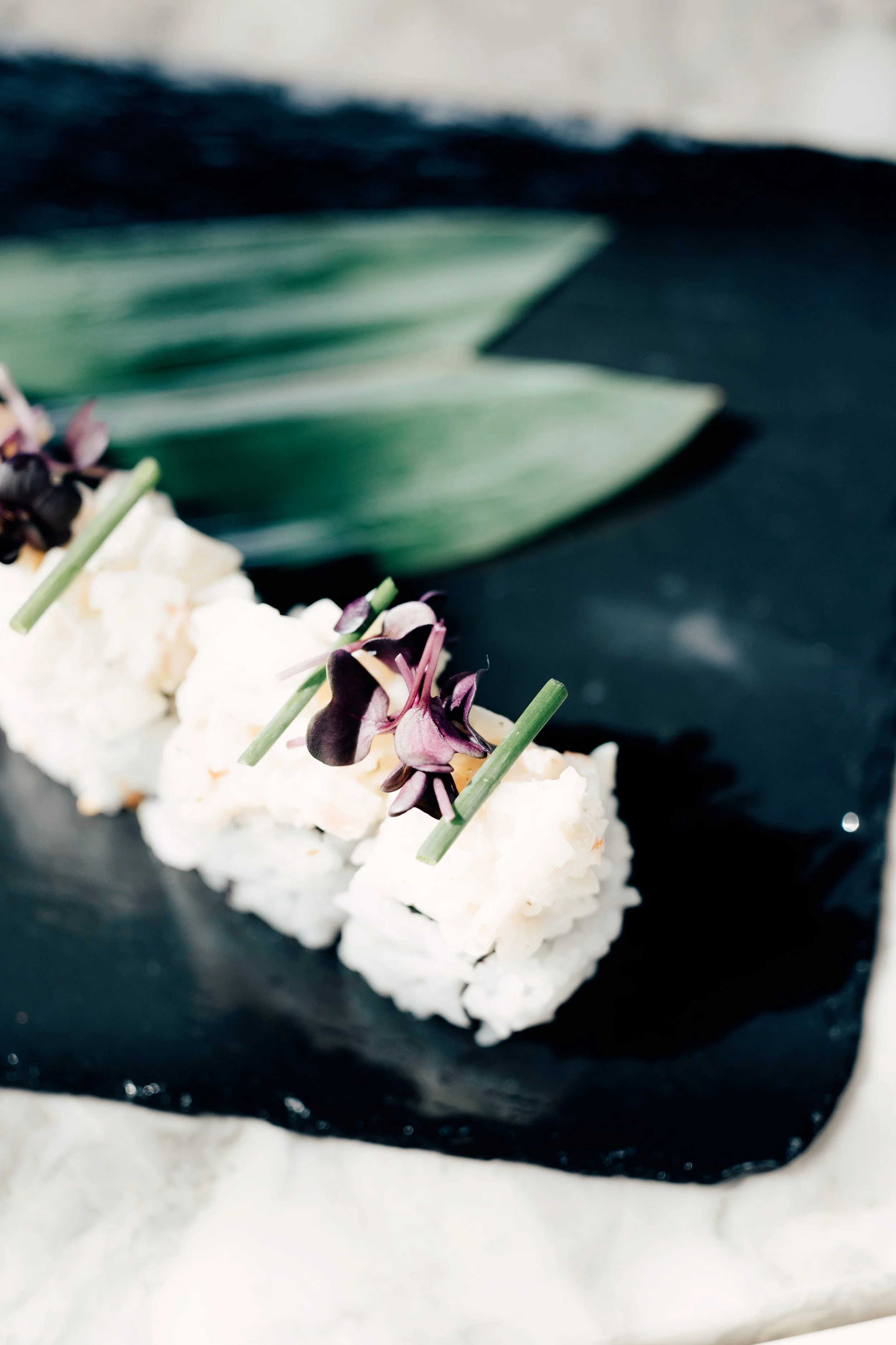 Sushi med dekorative blader og blomster på en svart plate.