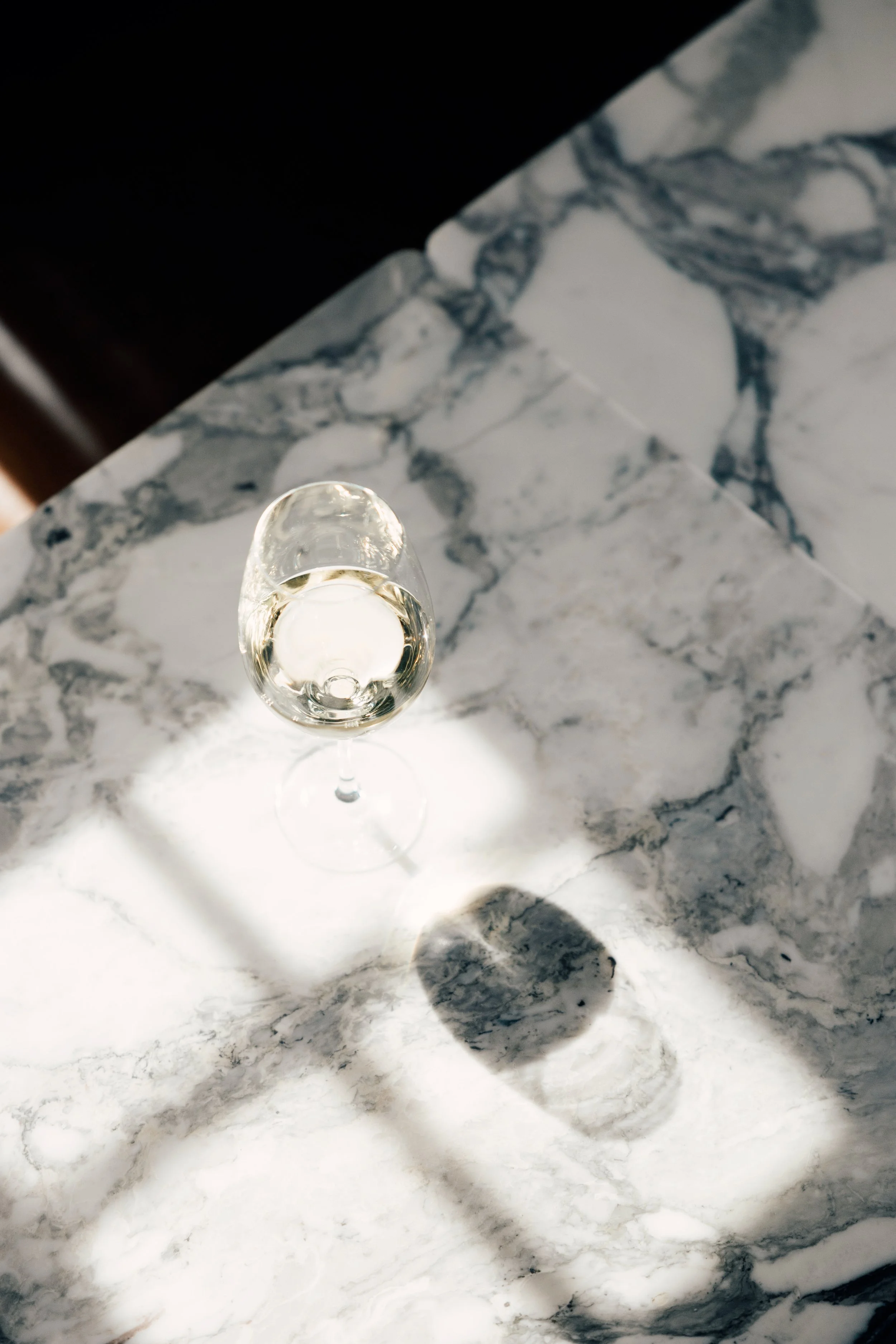 Et glass med hvitvin på en marmoroverflate med skygger.