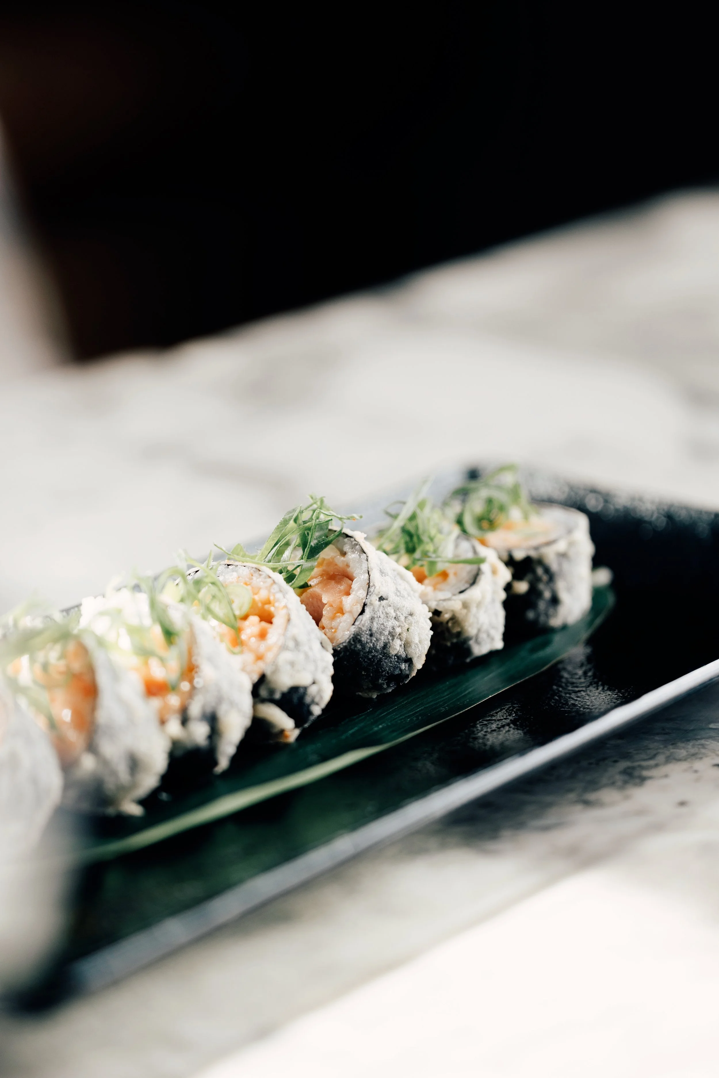 Sushi ruller med laks på et svart fat, pyntet med grønn løk.