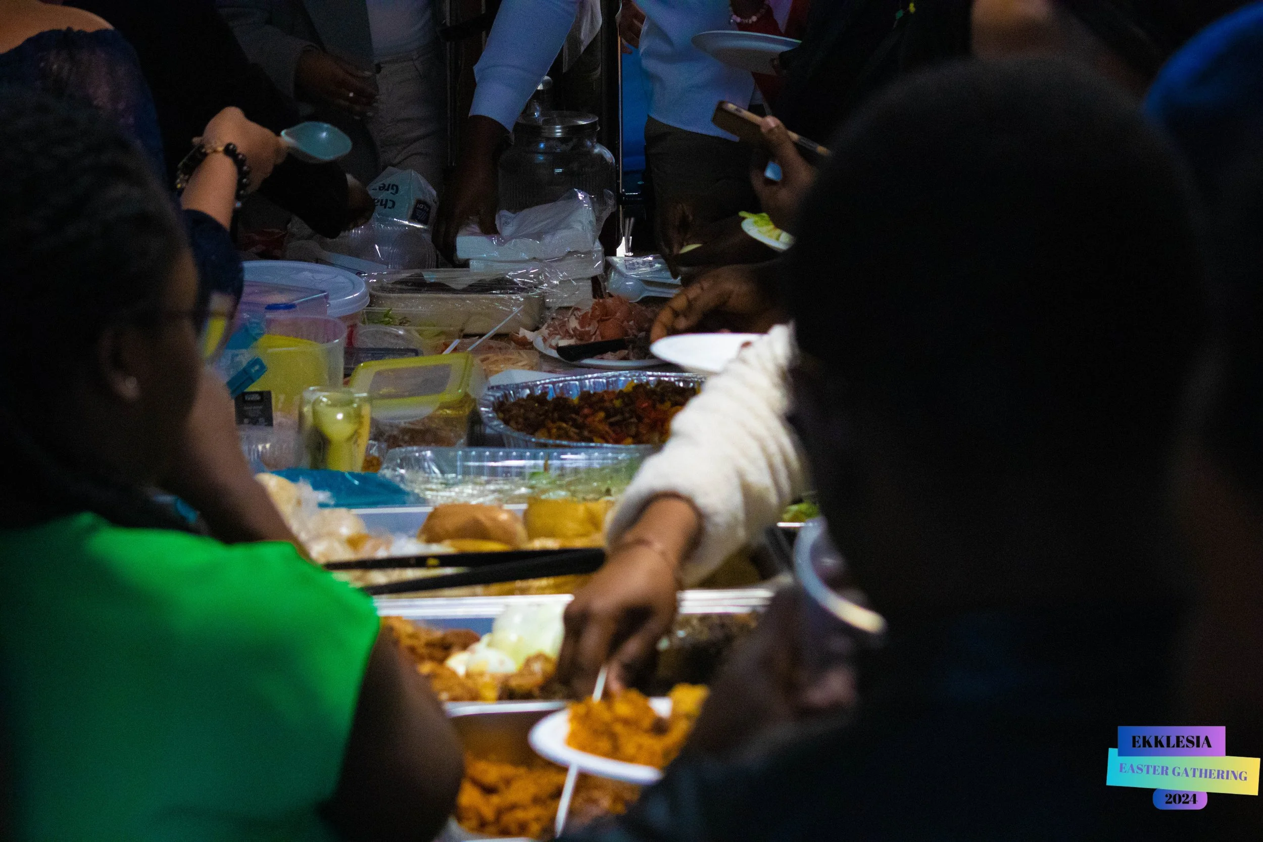 People gathered around a table sharing a meal with various dishes, serving themselves food at an Easter gathering.