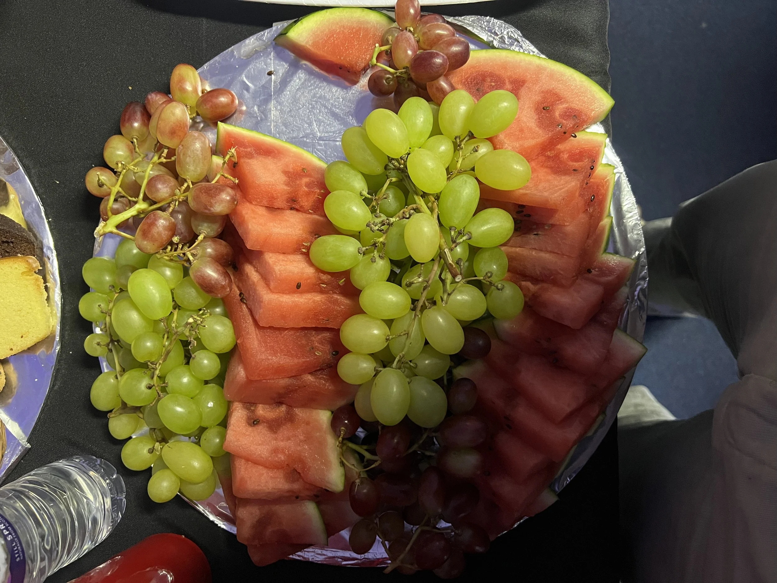A platter of sliced watermelon and red and green grapes on a foil-covered tray.