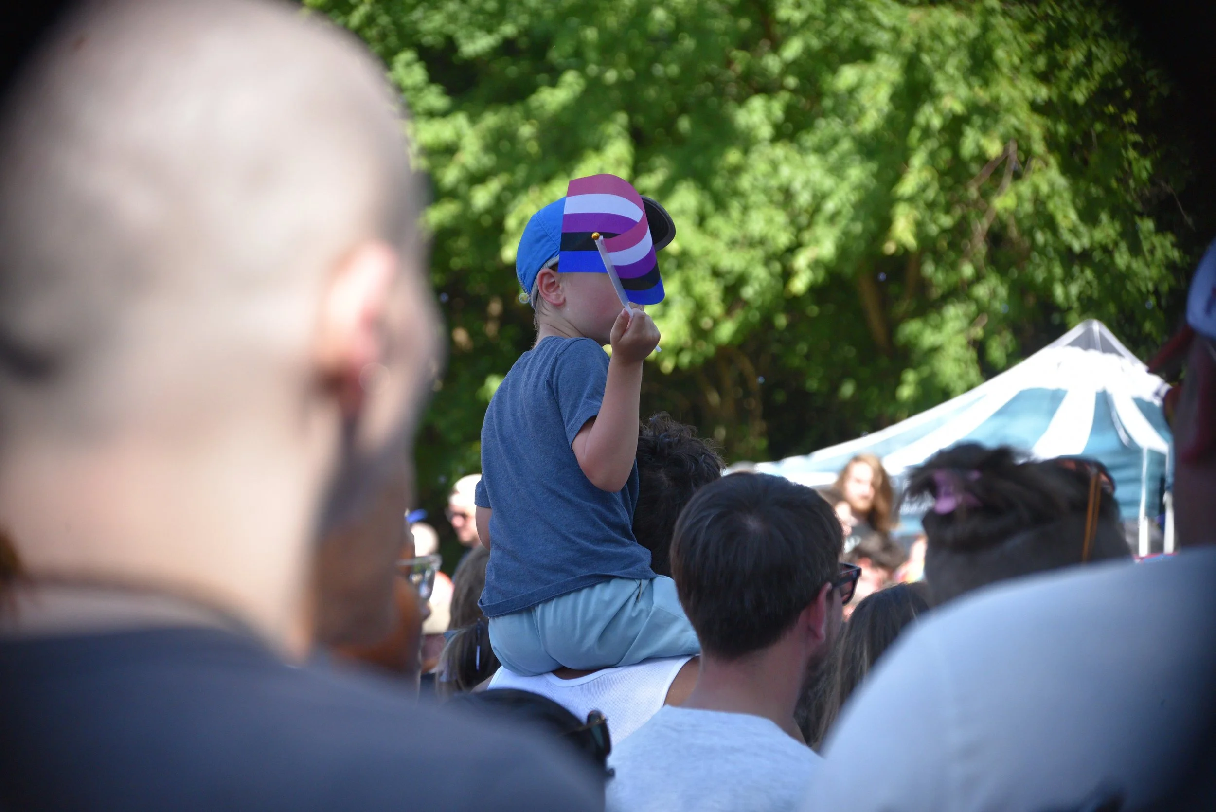 Child celebrating from atop an adult’s shoulders while waving a colorful Pride flag at SoKno Pride.