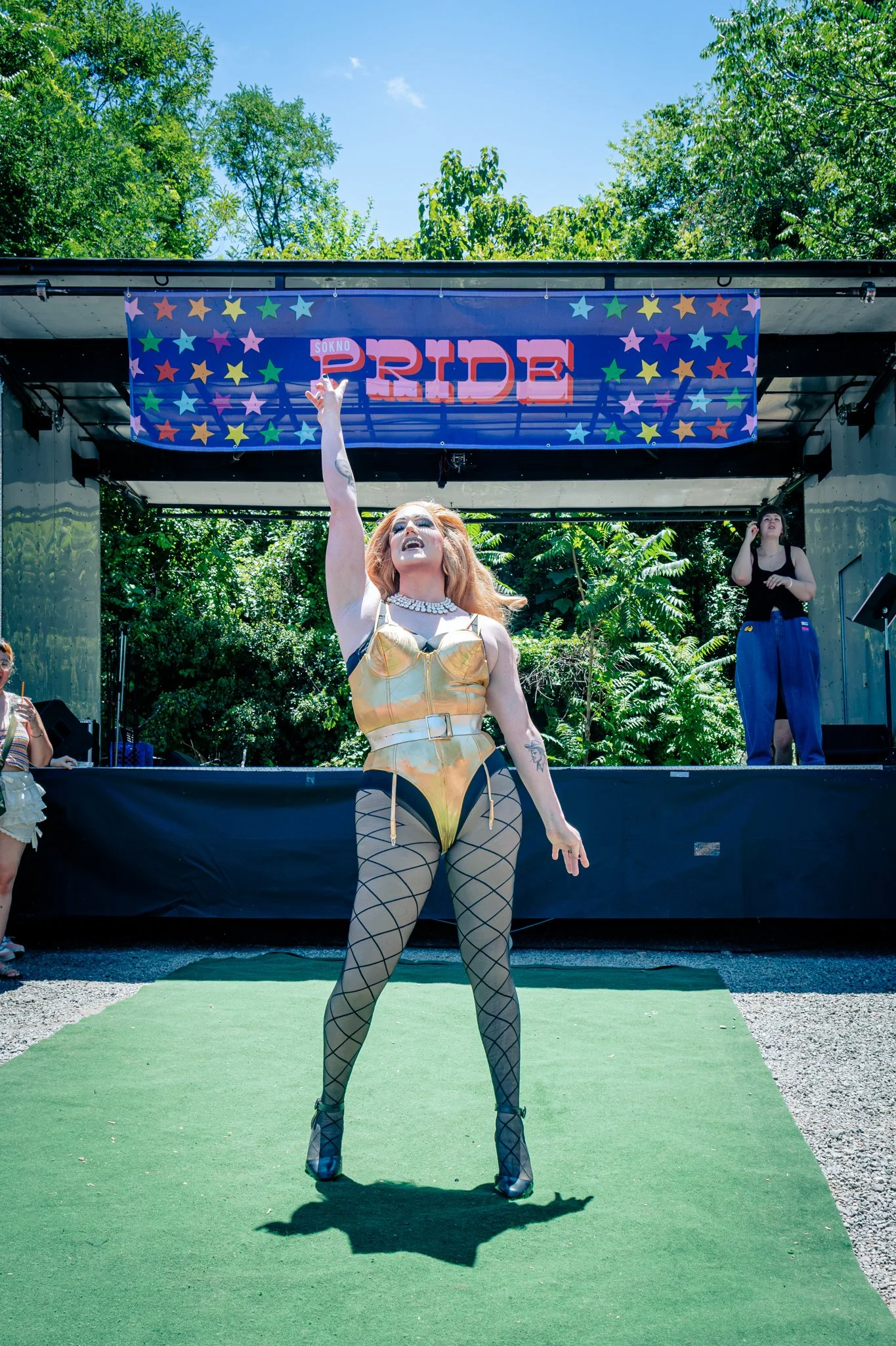 A drag entertainer commands the SoKno Pride 2026 stage in a gold costume as an ASL interpreter performs nearby.