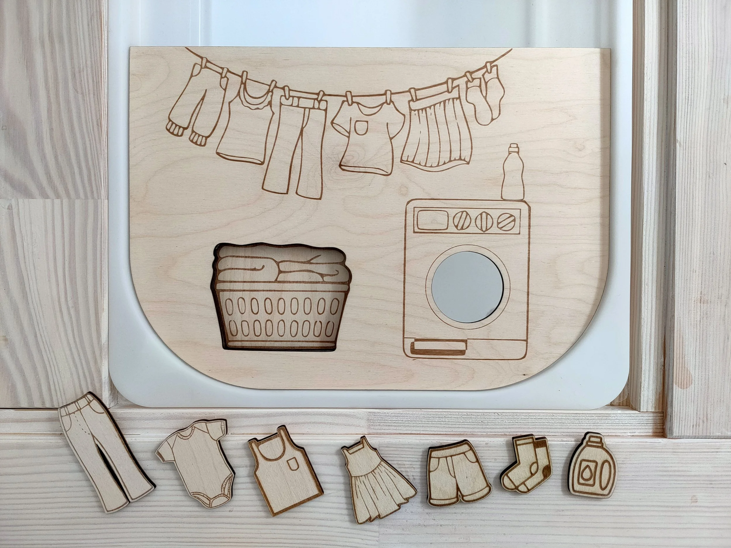 Illustration en bois représentant des vêtements et une machine à laver, avec des petits objets de vêtements en bois en dessous.