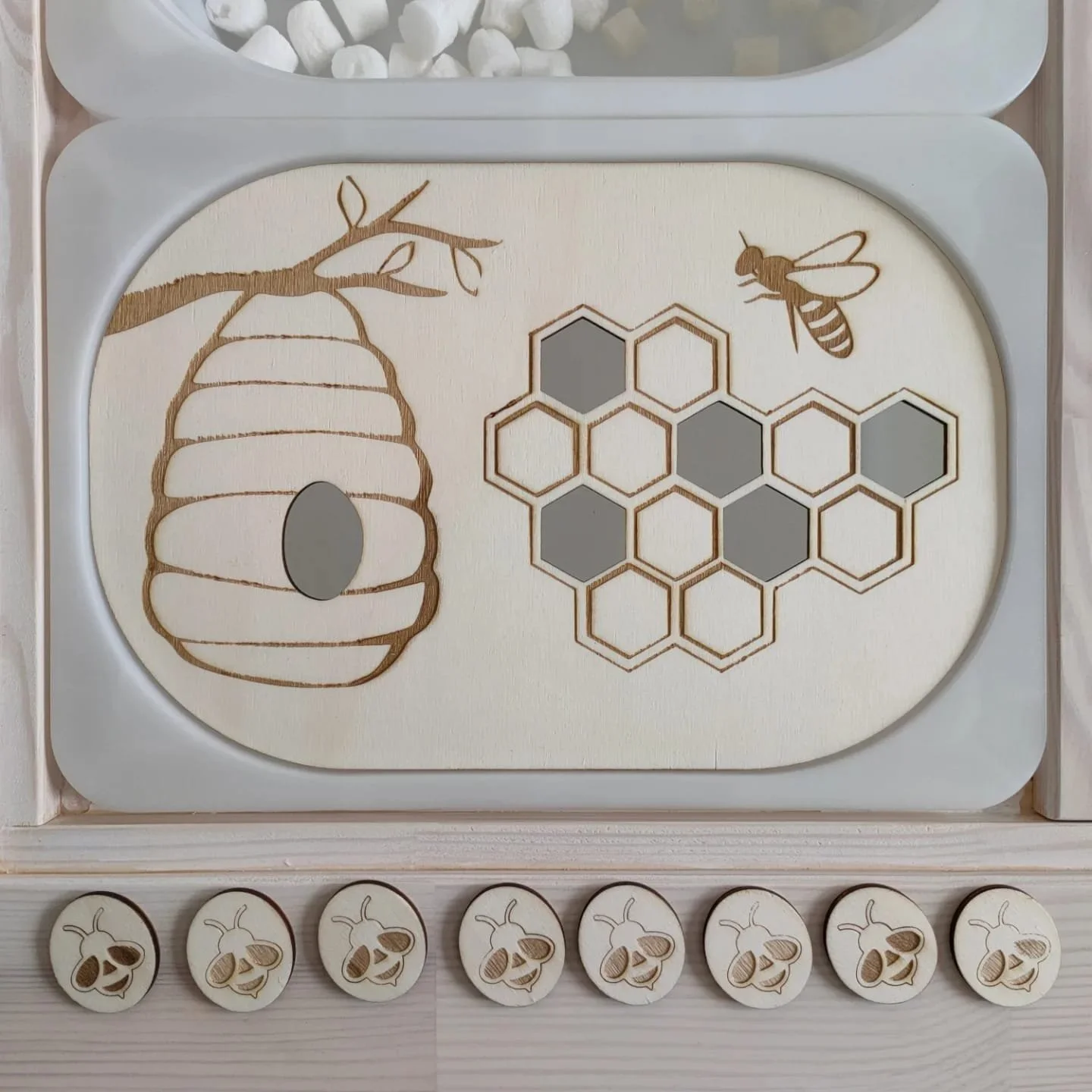 Plate en bois avec dessin d'une ruche, une abeille, et une grille hexagonale, avec des boutons en bois représentant des abeilles en dessous.