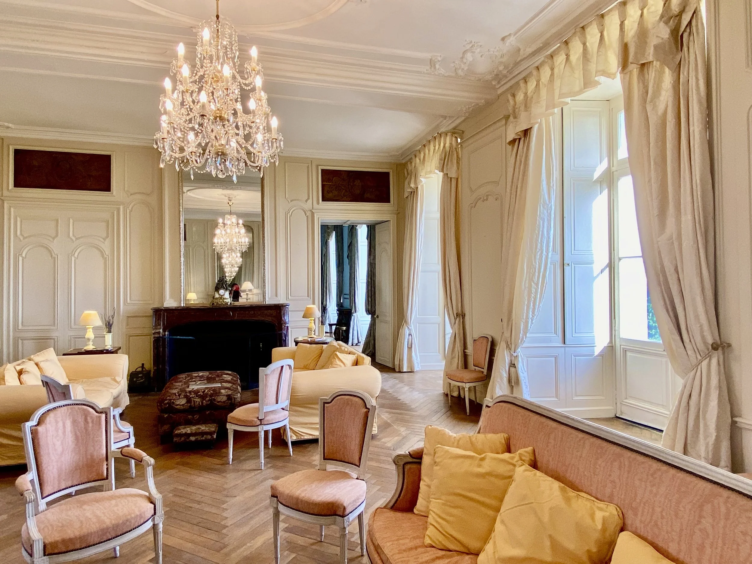 Elegant living room with chandeliers, cream-colored sofas, and large windows.