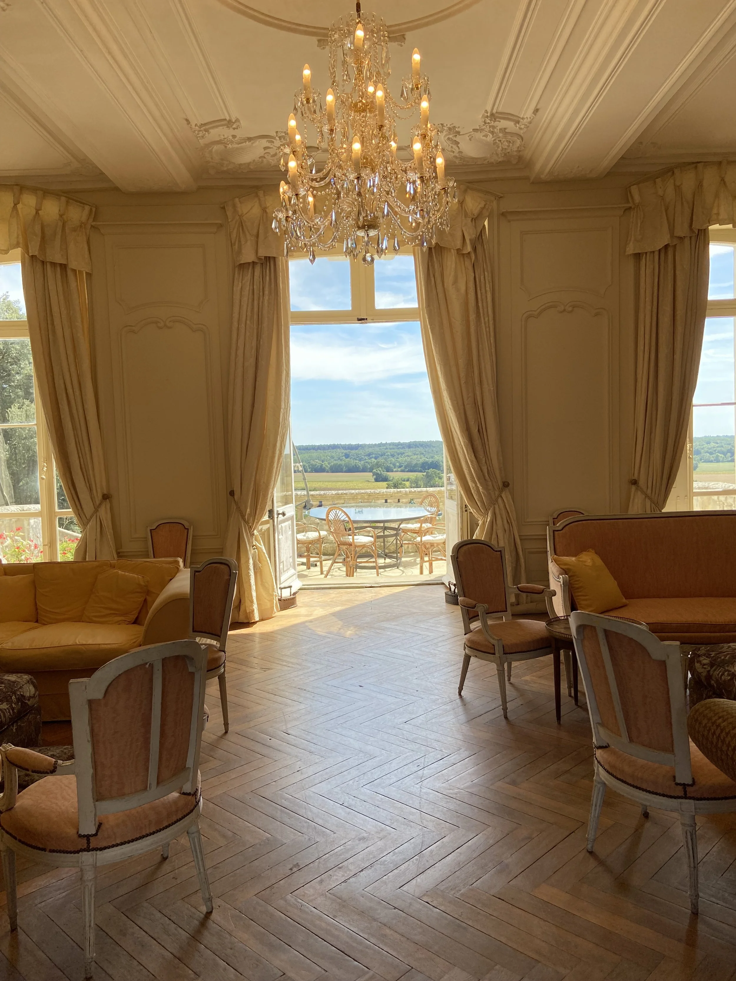 Elegant room with chandelier, vintage furniture, large windows, and outdoor view.