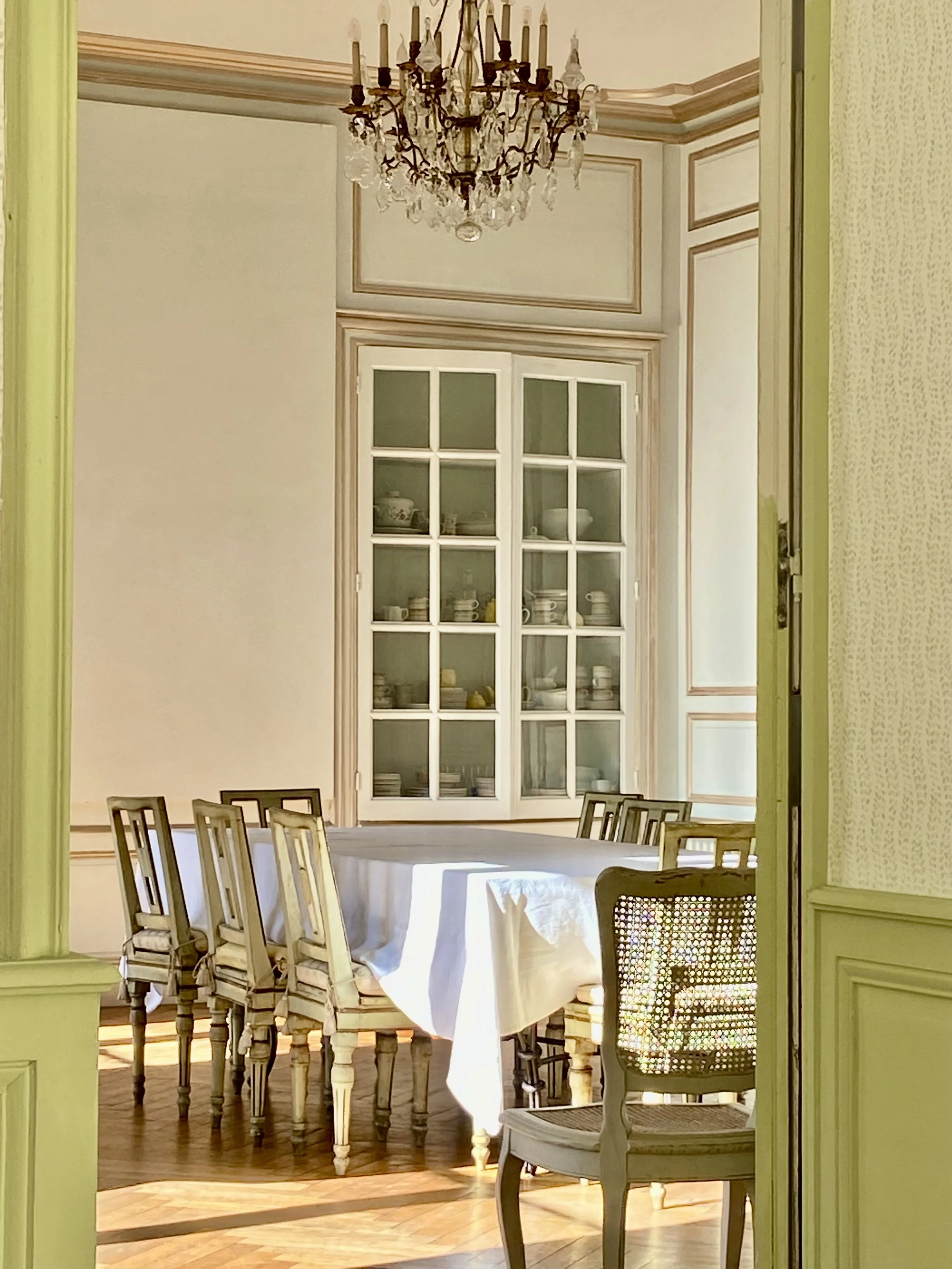 Elegant dining room with a chandelier, table with a white tablecloth, wooden chairs, and a glass cabinet with dishes.