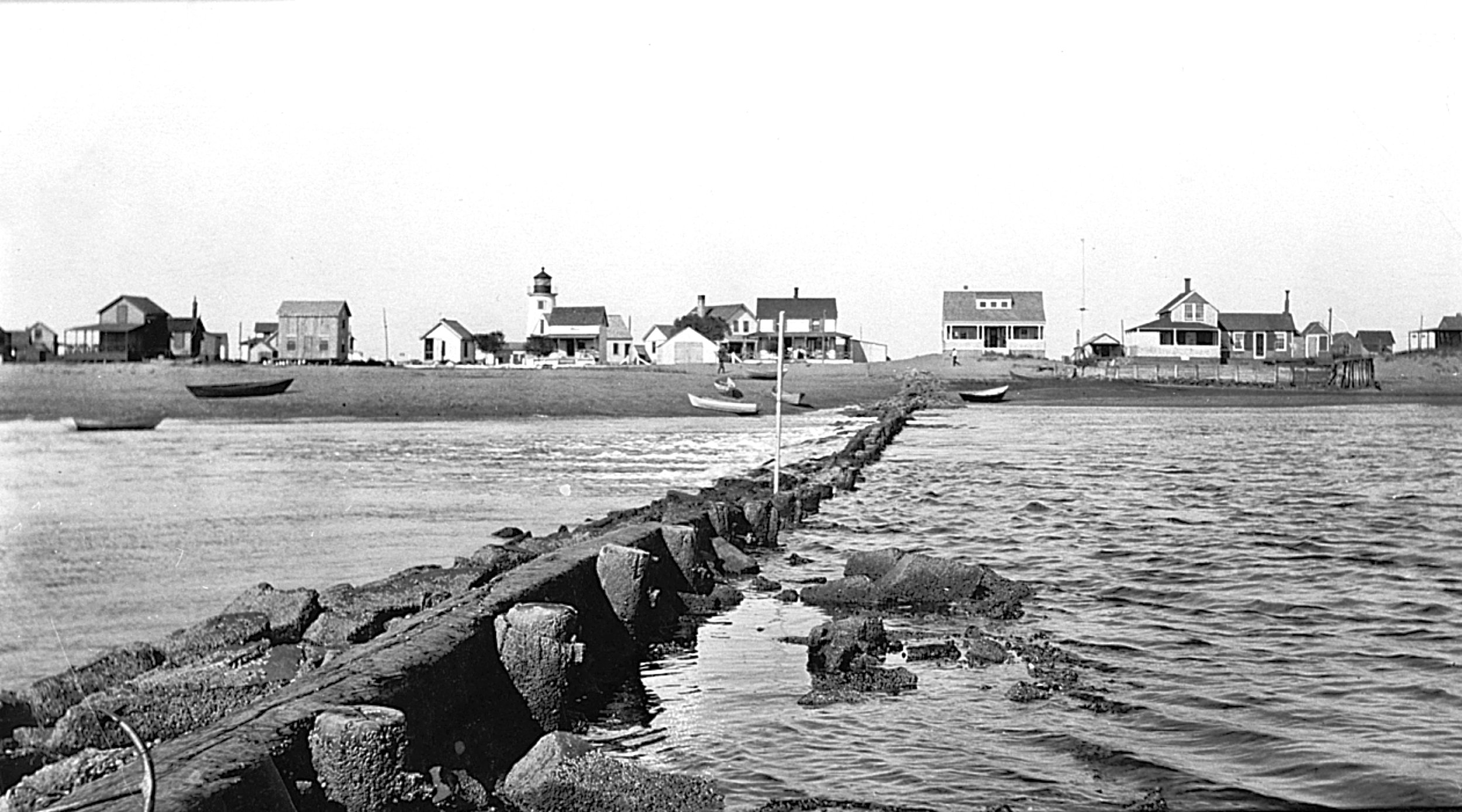 Dyke across the Basin… c1905;
A view of the “Dyke” as seen from the west side of the basin c 1905. The dyke was part of the river mouth jetty project starting on the Plum Island side in 1883 and completed in 1905. Its purpose was to discourage the r