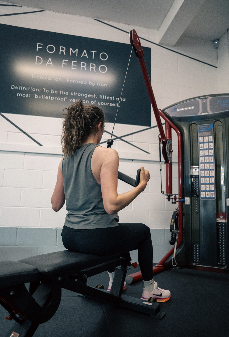 A woman sitting on a workout bench using a cable machine for strength training at The Ferraro Method personal training studio in Hitchin.