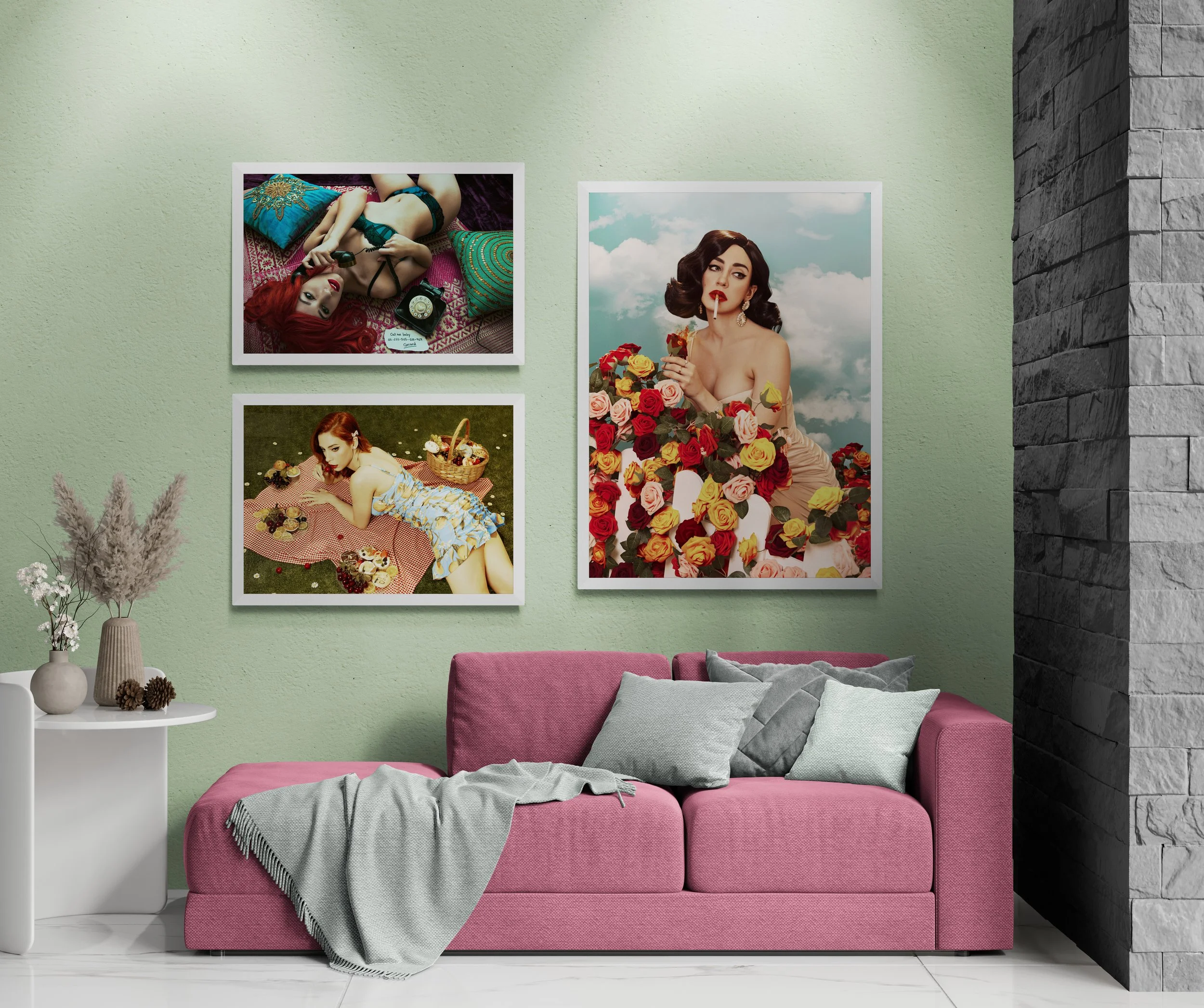 A living room with a pink sofa and light green walls, adorned with three framed vintage-style photos. One features a woman with red hair in lingerie, another depicts a woman in a floral dress with picnic baskets, and the third shows a woman surrounded by colorful roses. Decorative plants and vases are placed on a side table.