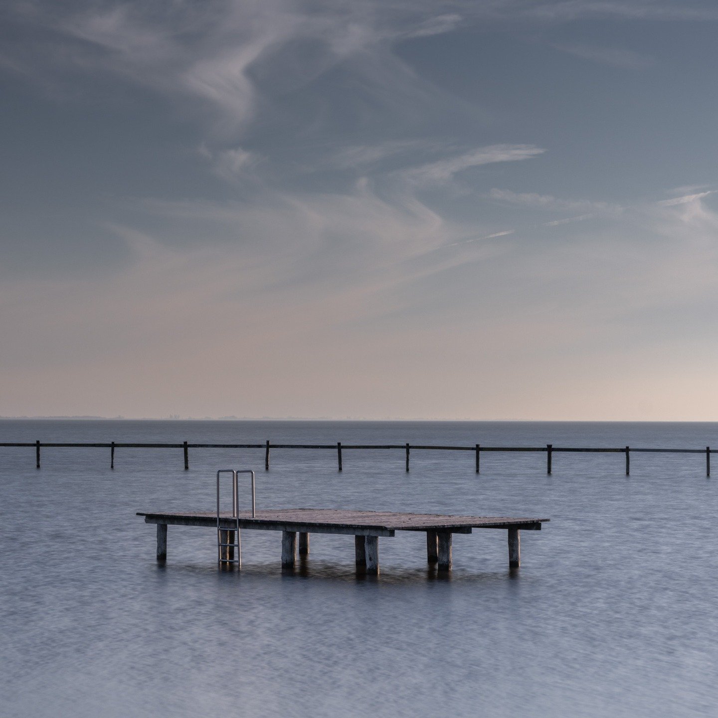 Dawn breaks over one of Europe's unique steppe lakes, casting the wooden pier into soft twilight tones. The Neusiedlersee, straddling Austria and Hungary, is known for its shallow waters and endless reed belts. Here at Breitbrunn, the landscape speak