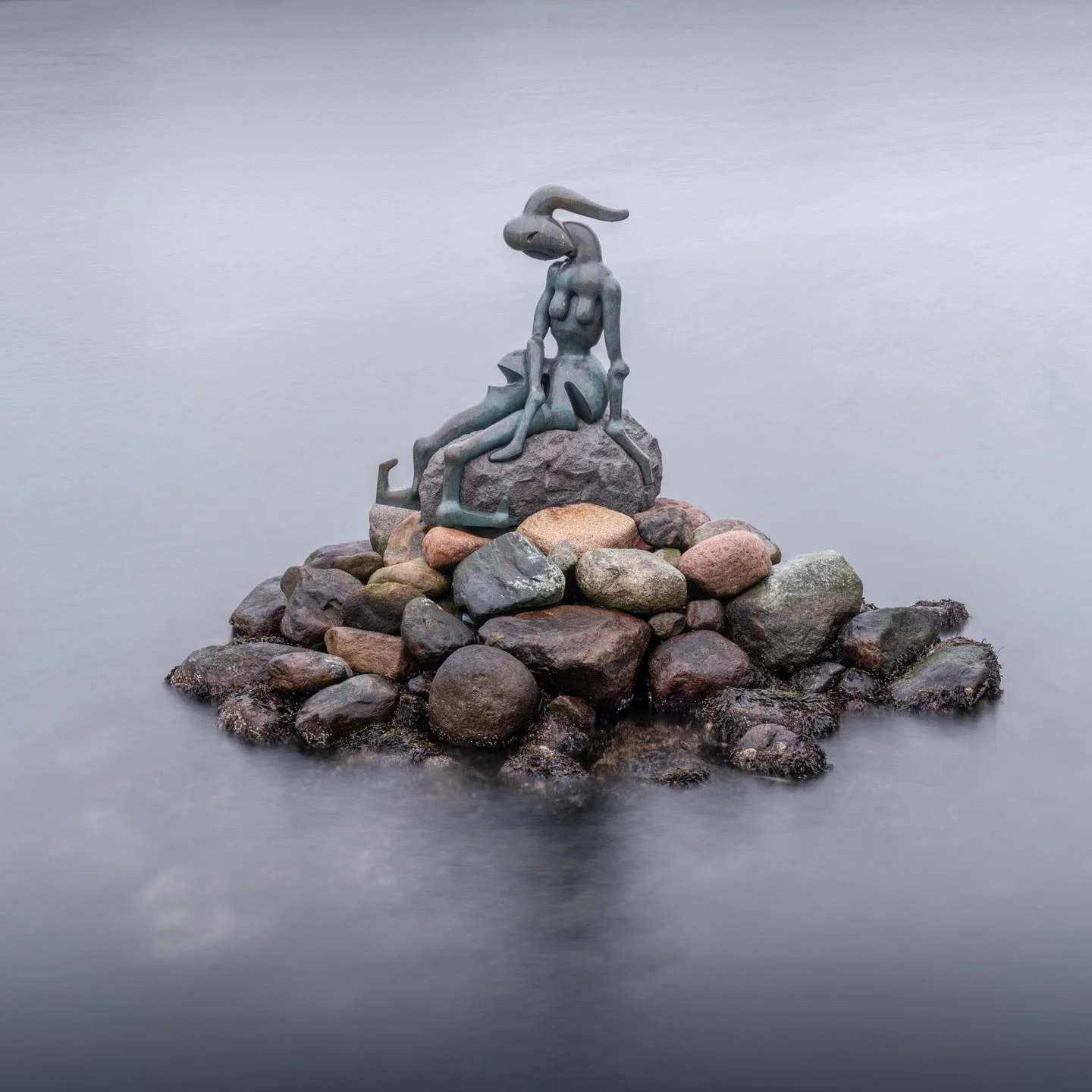 Most visitors never find her. While crowds gather around Edvard Eriksen&rsquo;s romantic Little Mermaid, this distorted figure rests alone on weathered stones in Dahlerups Square. Professor Bj&oslash;rn N&oslash;rgaard sculpted her with elongated lim