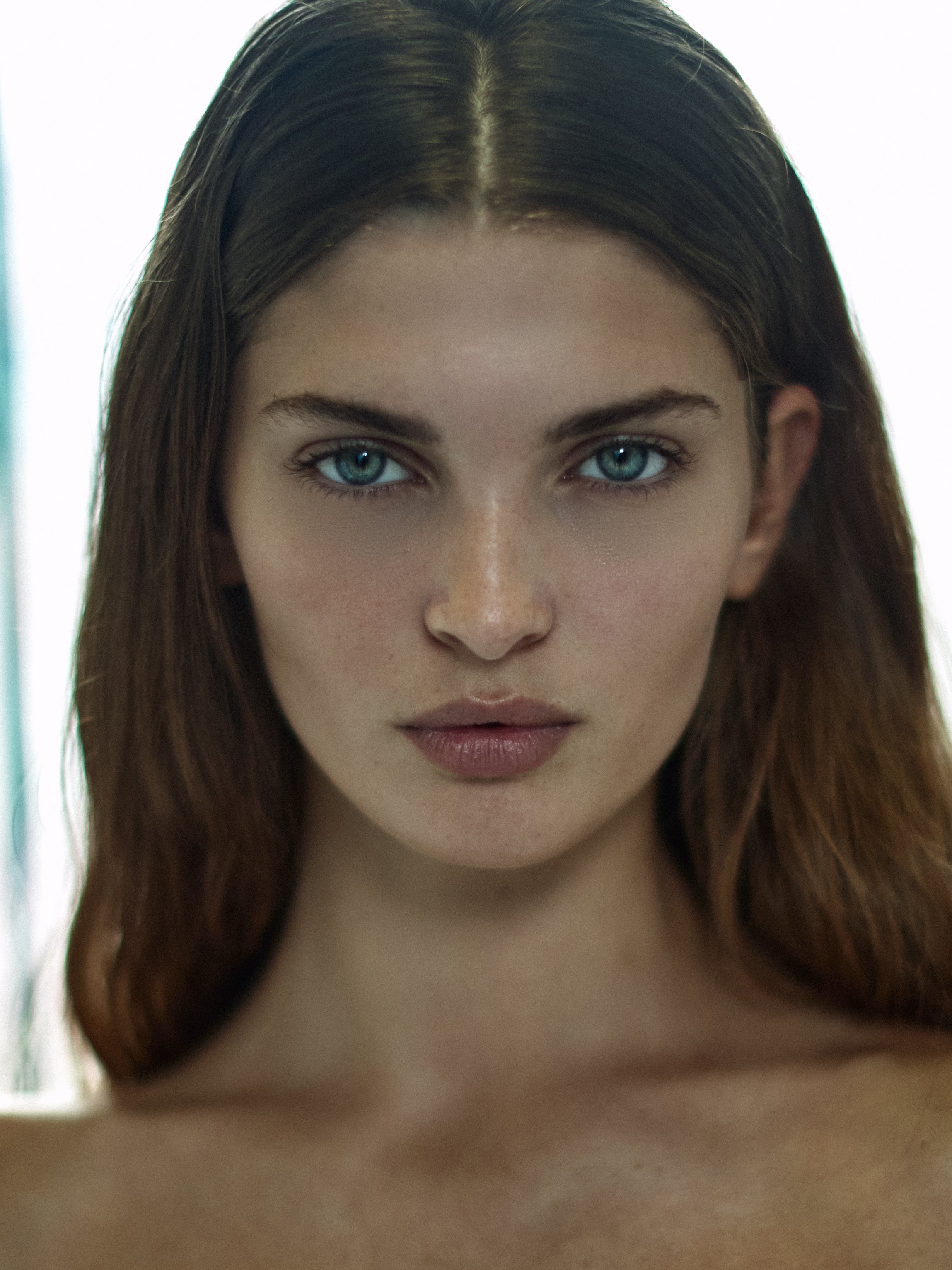 Close-up of a young woman's face with blue eyes and long brown hair, with her lower face and chin slightly out of focus.