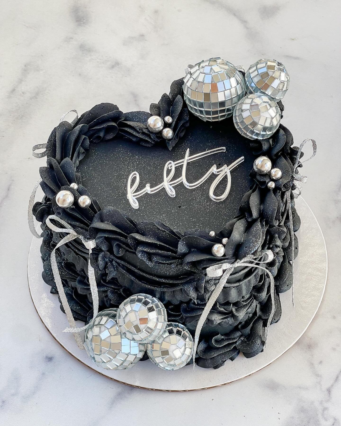 nothing but the best for @the_foodie_board 🖤🪩

&bull; 6&rdquo; two layer heart cake with black buttercream, black piping, edible silver glitter, disco balls, silver bows &amp; @floraldust_ acrylic cake charm ✨
&bull; custom cupcakes with @floraldus