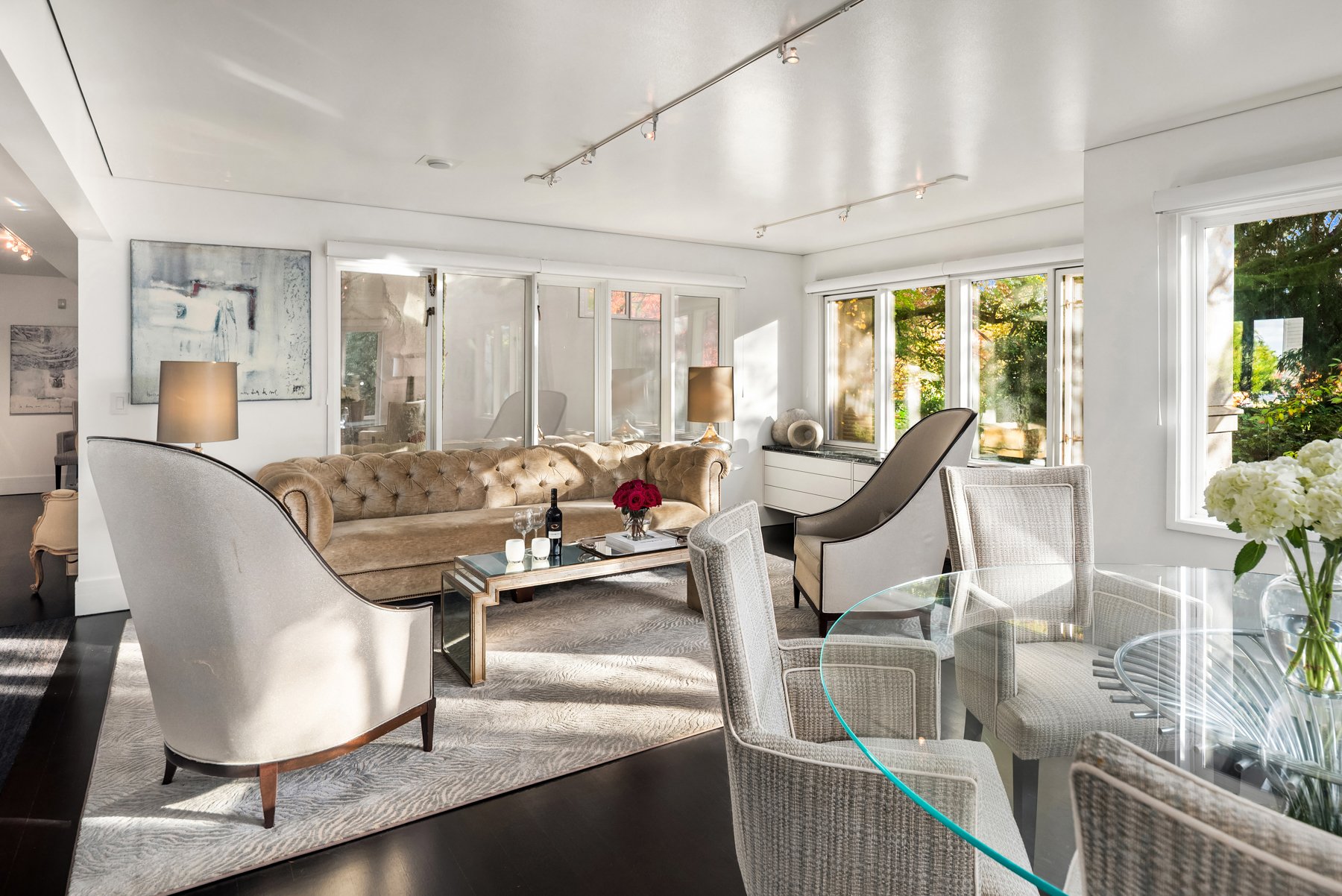 A large, well-maintained house with a tiled roof, surrounded by lush green trees and manicured lawn, with a curved driveway leading up to it. In the background, there are tall forests and a view of a blue body of water under a clear sky.