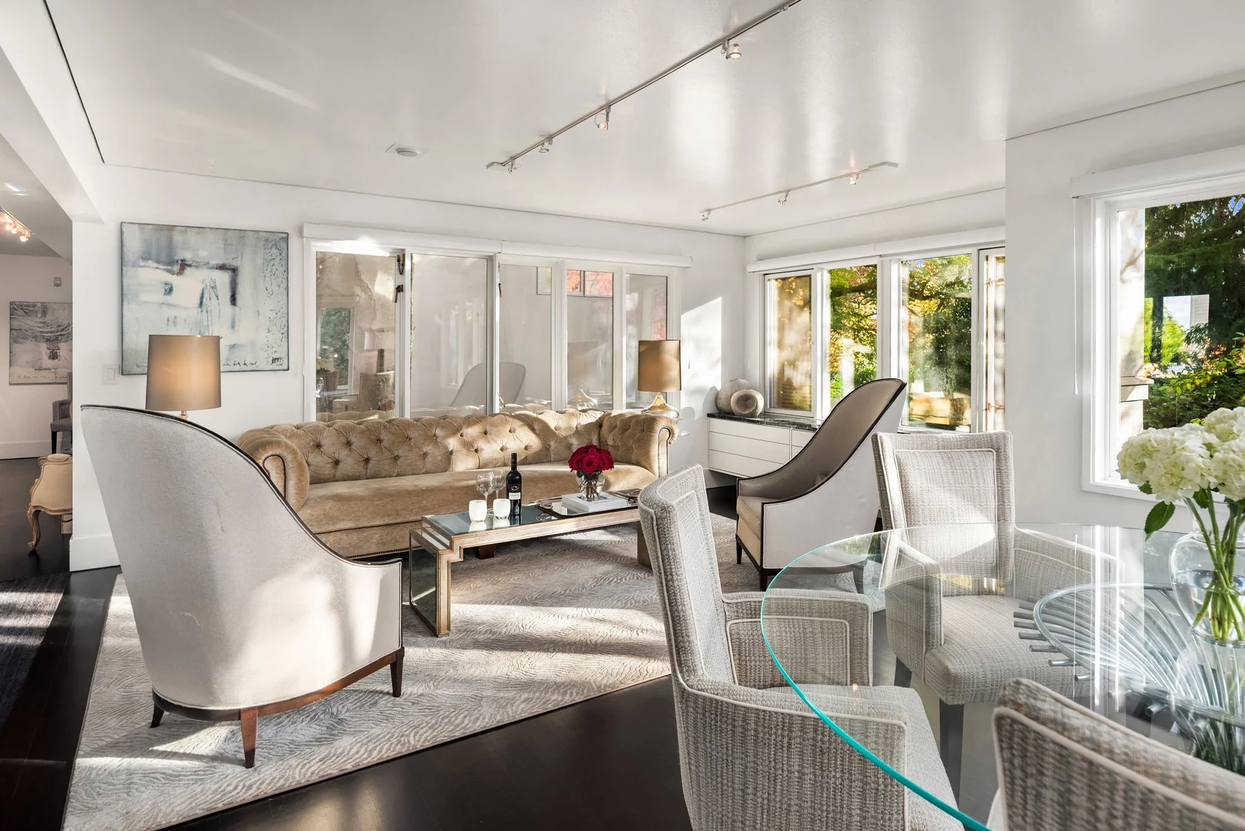 A large, well-maintained house with a tiled roof, surrounded by lush green trees and manicured lawn, with a curved driveway leading up to it. In the background, there are tall forests and a view of a blue body of water under a clear sky.