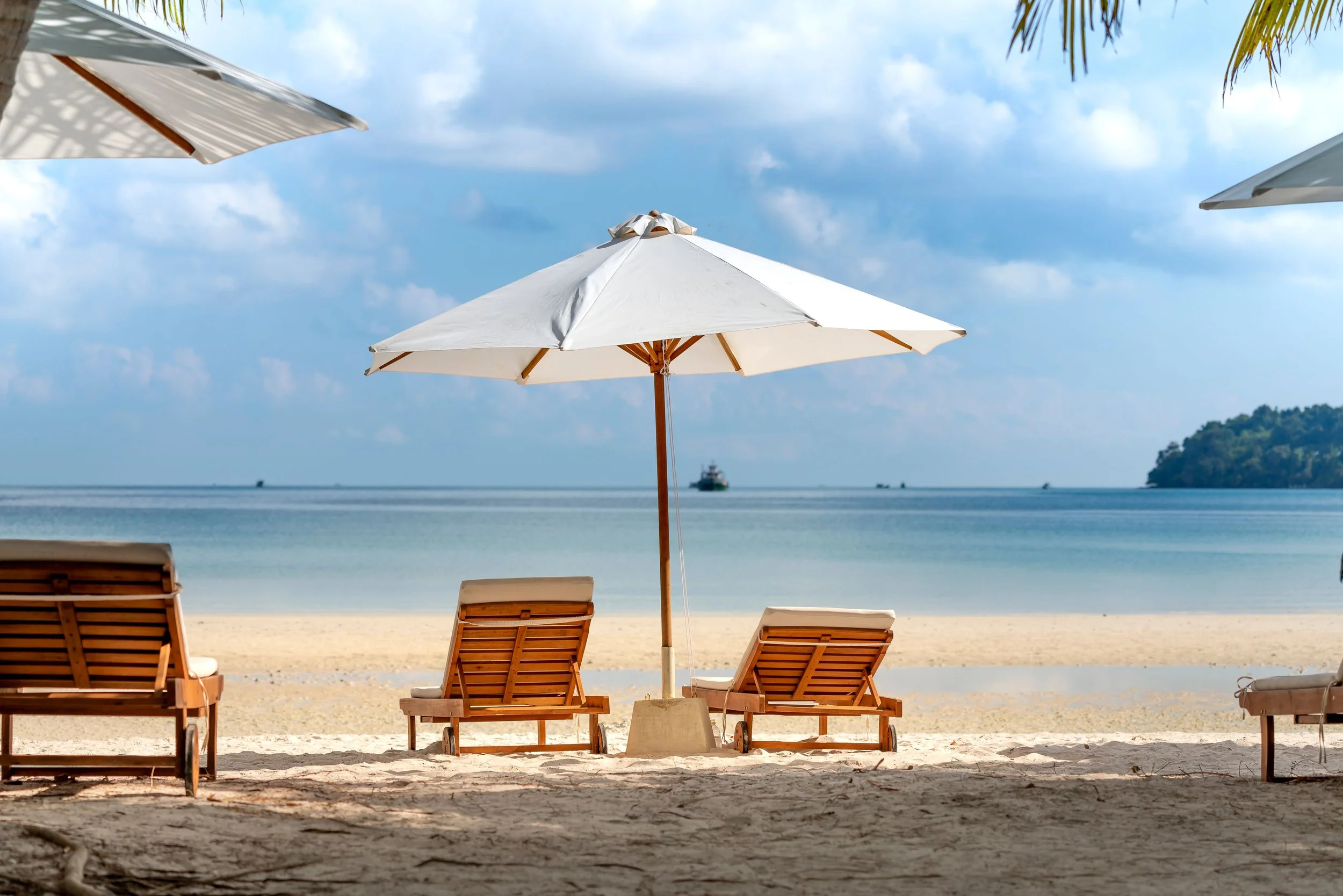 Reclining chairs on a beach underneath a white umbrella on a tropical island looking out to the ocean..