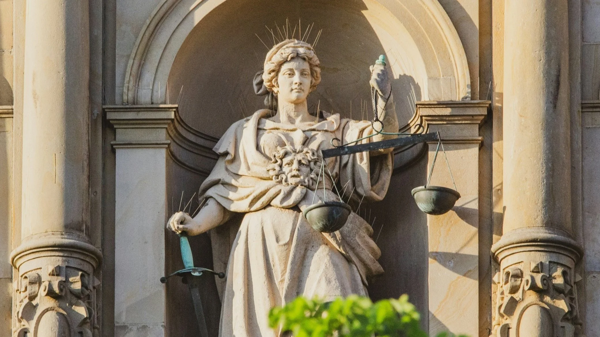Statue of Lady Justice holding a sword and scales, with a crown of rays, on a building facade.