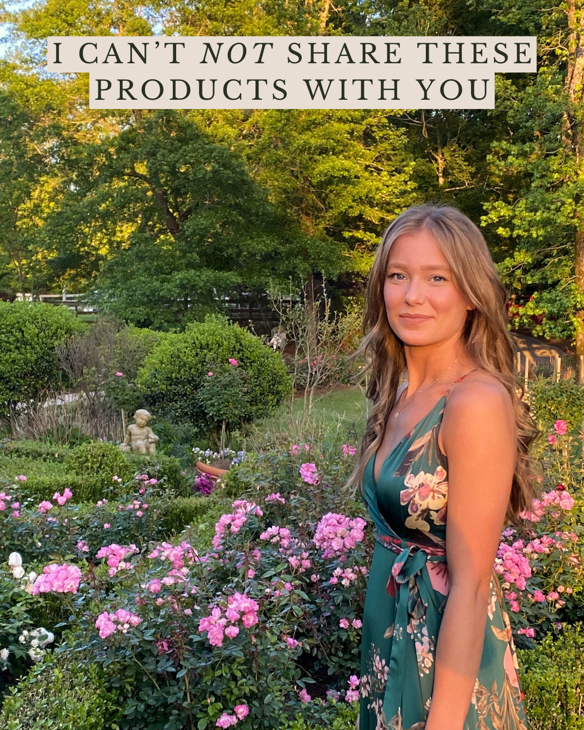 A woman with long, wavy hair stands among pink roses in a garden with greenery and trees in the background. The photo is taken outdoors during sunset.