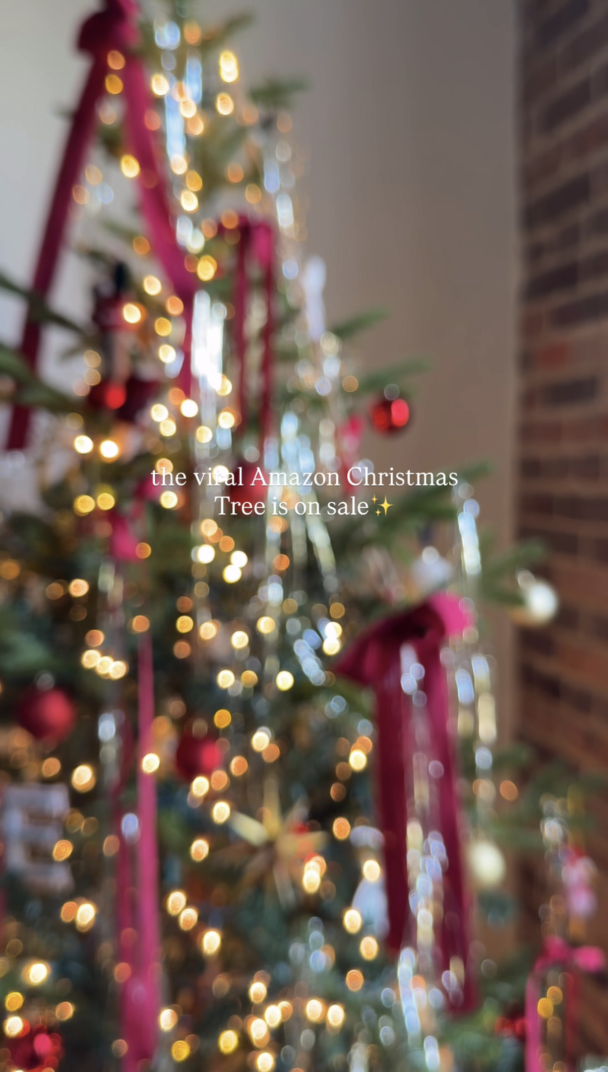 Blurred Christmas tree decorated with lights and ornaments, with a brick wall in the background. Text overlay says: "the viral Amazon Christmas Tree is on sale".