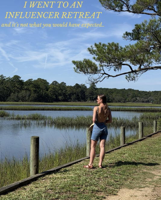 A woman stands by a wooden fence along a river or lake, looking at the water and trees under a clear blue sky, with the phrase 'I WENT TO AN INFLUENCER RETREAT and it's not what you would have expected...' written in yellow text at the top.