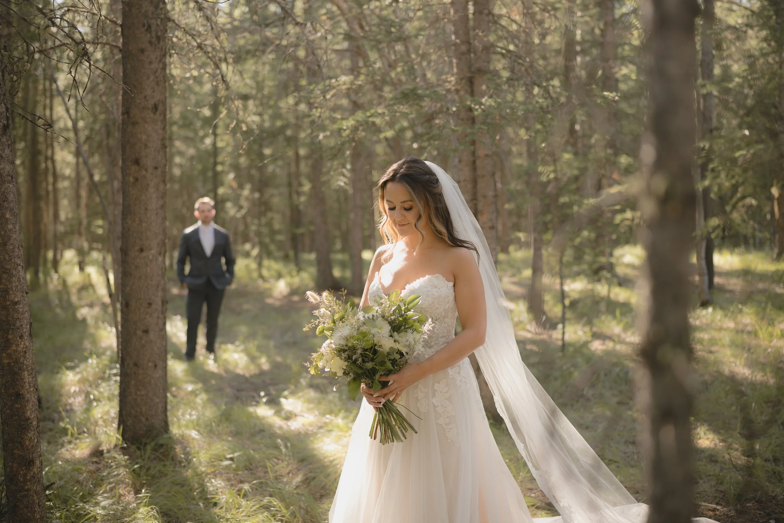 Kananaskis Wedding. Bride in forefront holding bouquet, groom in background admiring her.