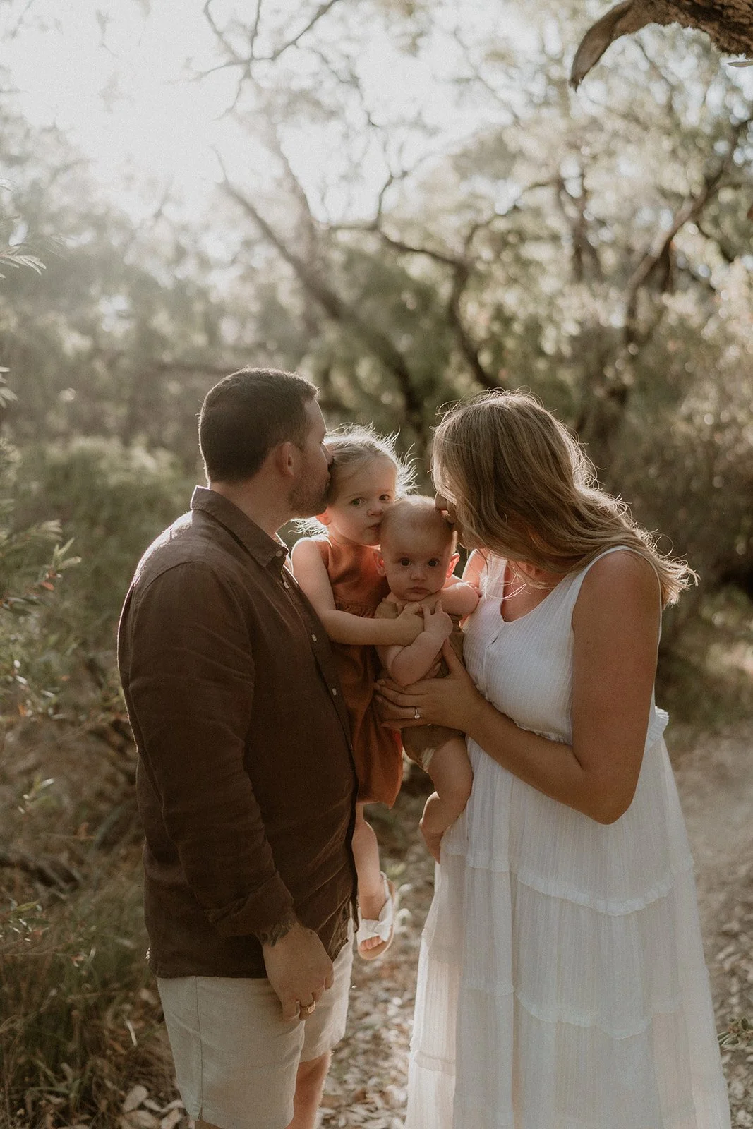 A couple happily getting engaged at Eagle Bay Beach, surrounded by a luxurious white picnic setup including a fringed umbrella, deck chairs, and rattan coffee table.