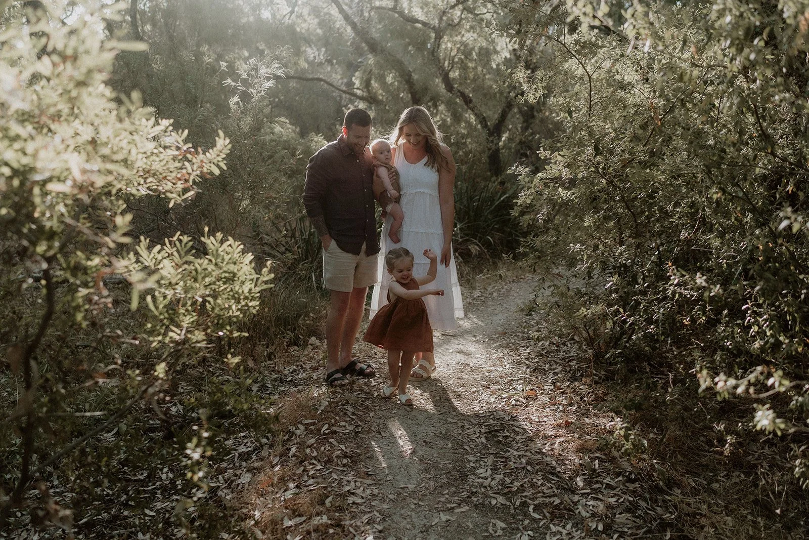A couple happily getting engaged at Eagle Bay Beach, surrounded by a luxurious white picnic setup including a fringed umbrella, deck chairs, and rattan coffee table.
