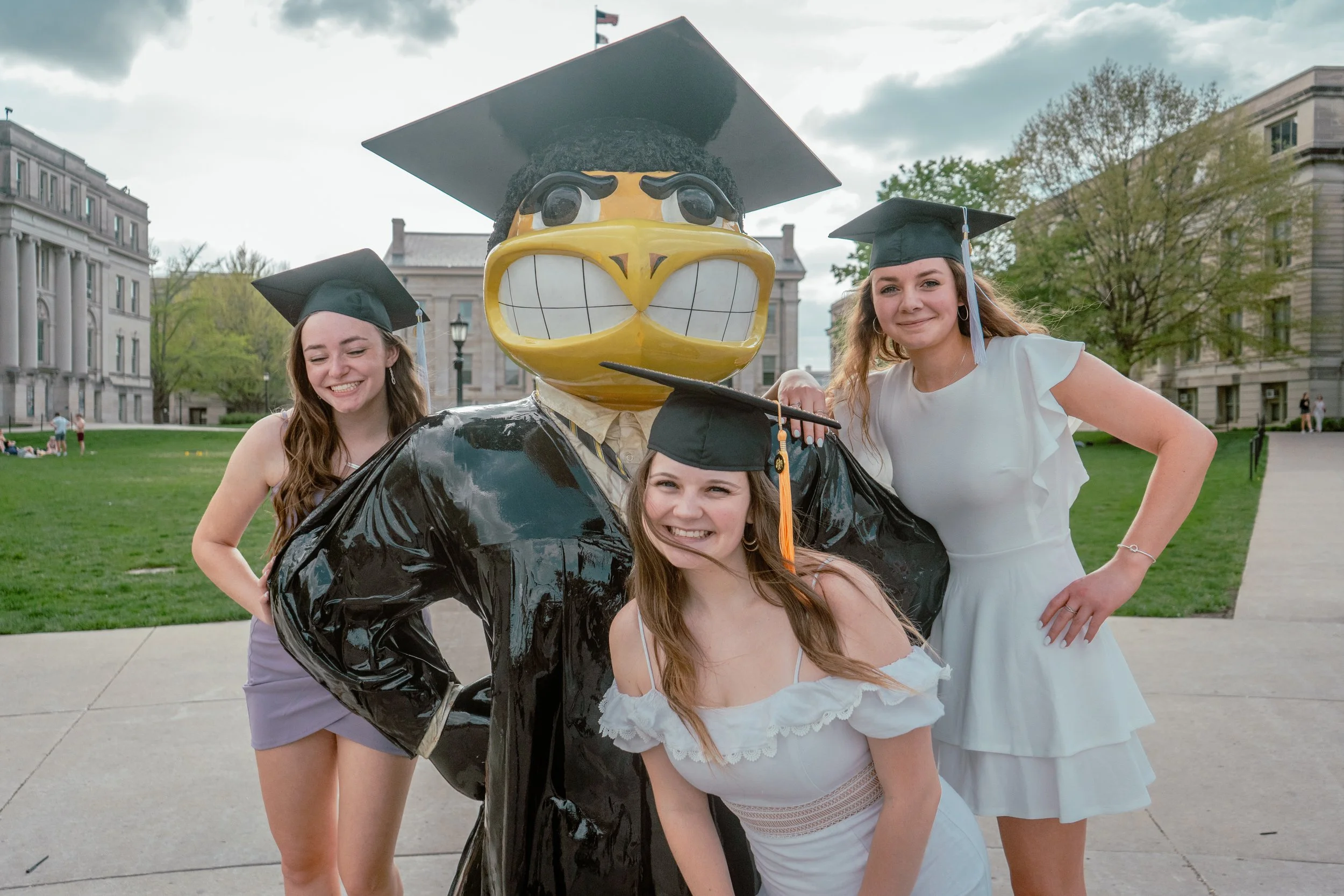 A GROUP OF 3 WOMEN TAKE GRADUATION PHOTO ON THE UNIVERSITY OF IOWA CAMPUS TO CELEBRATE THE MOMENT