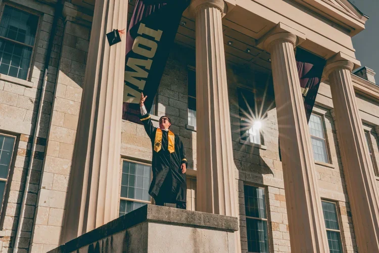 IOWA CITY SENIOR PORTRAIT SESSION - UNIVERSITY OF IOWA GRAD PHOTO ON THE STEPS OF THE OLD CAPITAL BUILDING, HE IS THROWING HIS HAT INTO THE AIR