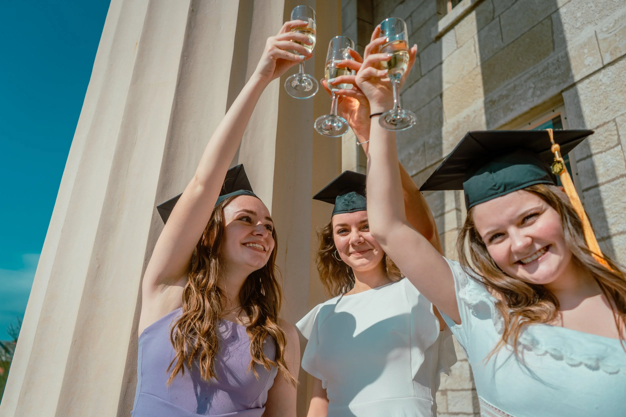 A GROUP OF 3 WOMEN TAKE GRADUATION PHOTO ON THE UNIVERSITY OF IOWA CAMPUS TO CELEBRATE THE MOMENT