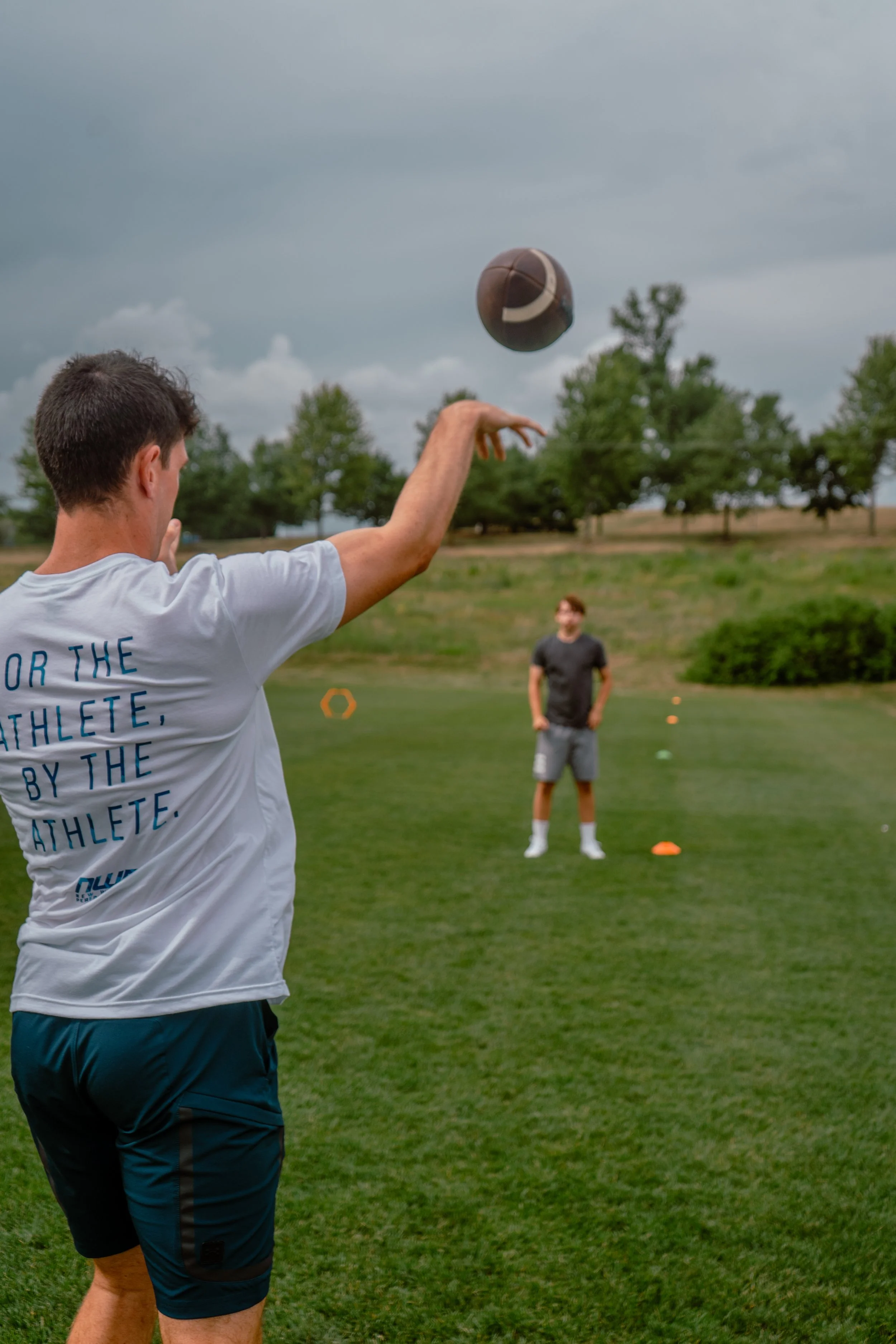 A COACH THROWS A FOOTBALL AT HIS ATHLETE