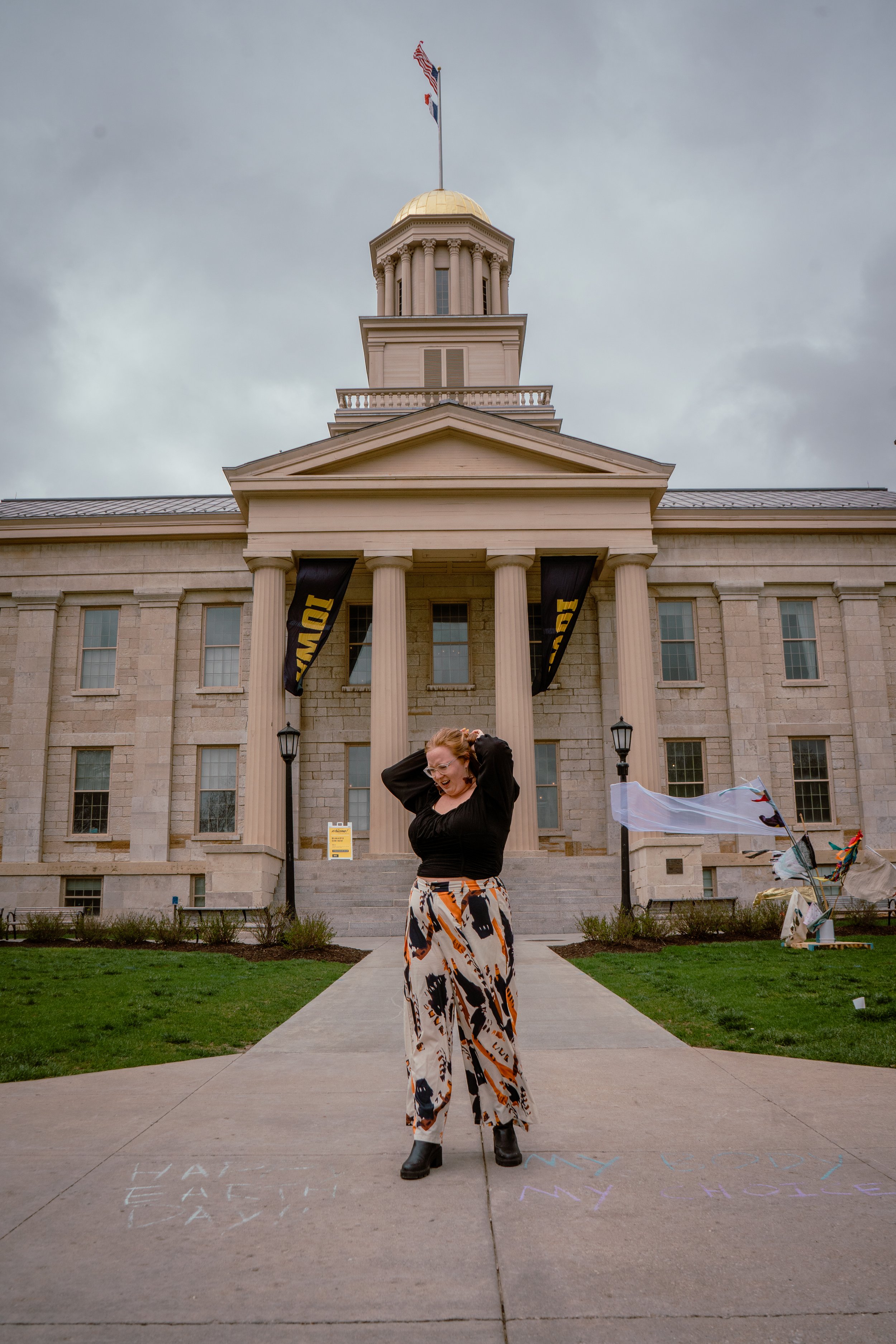 A WOMEN STANDING OUTSIDE OF THE UNIVERSITY IOWA OLD CAPITAL BUILDING FOR GRADUATION PHOTOS