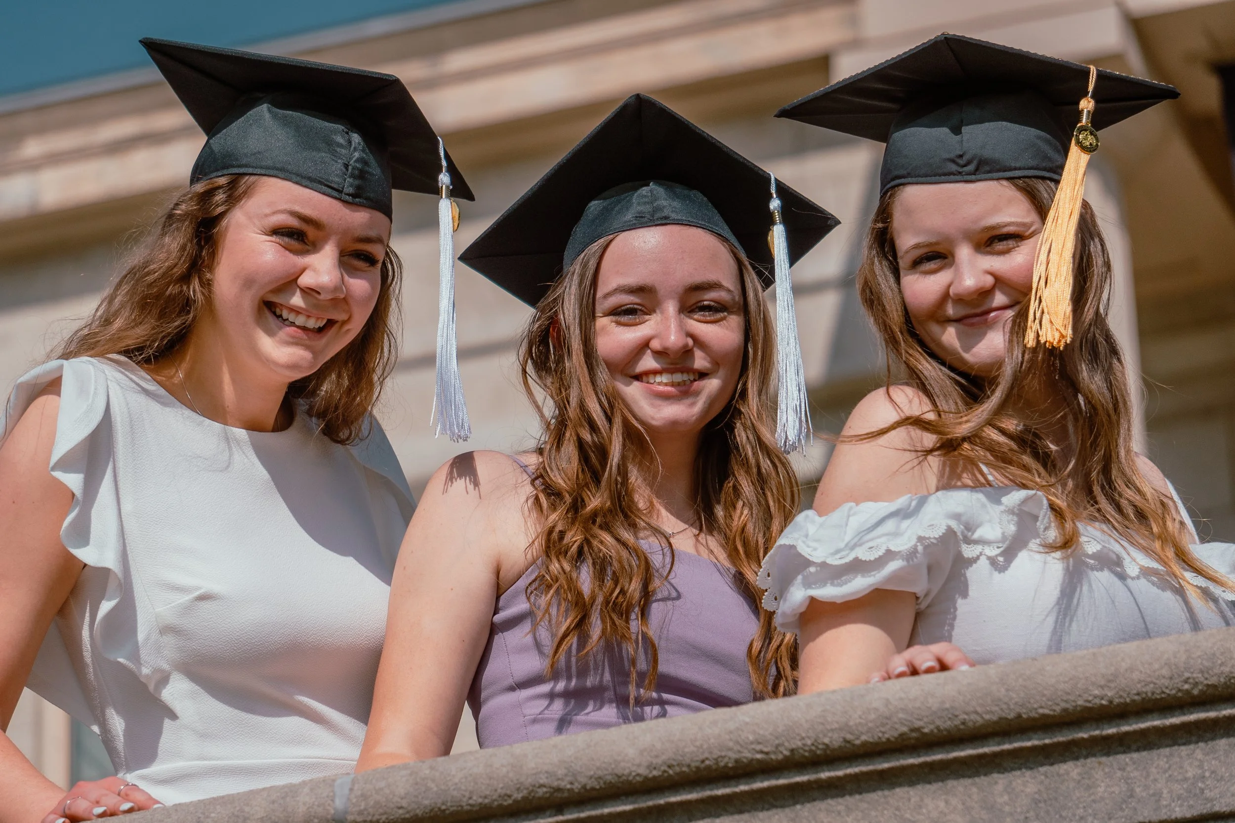 A GROUP OF 3 WOMEN TAKE GRADUATION PHOTO ON THE UNIVERSITY OF IOWA CAMPUS TO CELEBRATE THE MOMENT