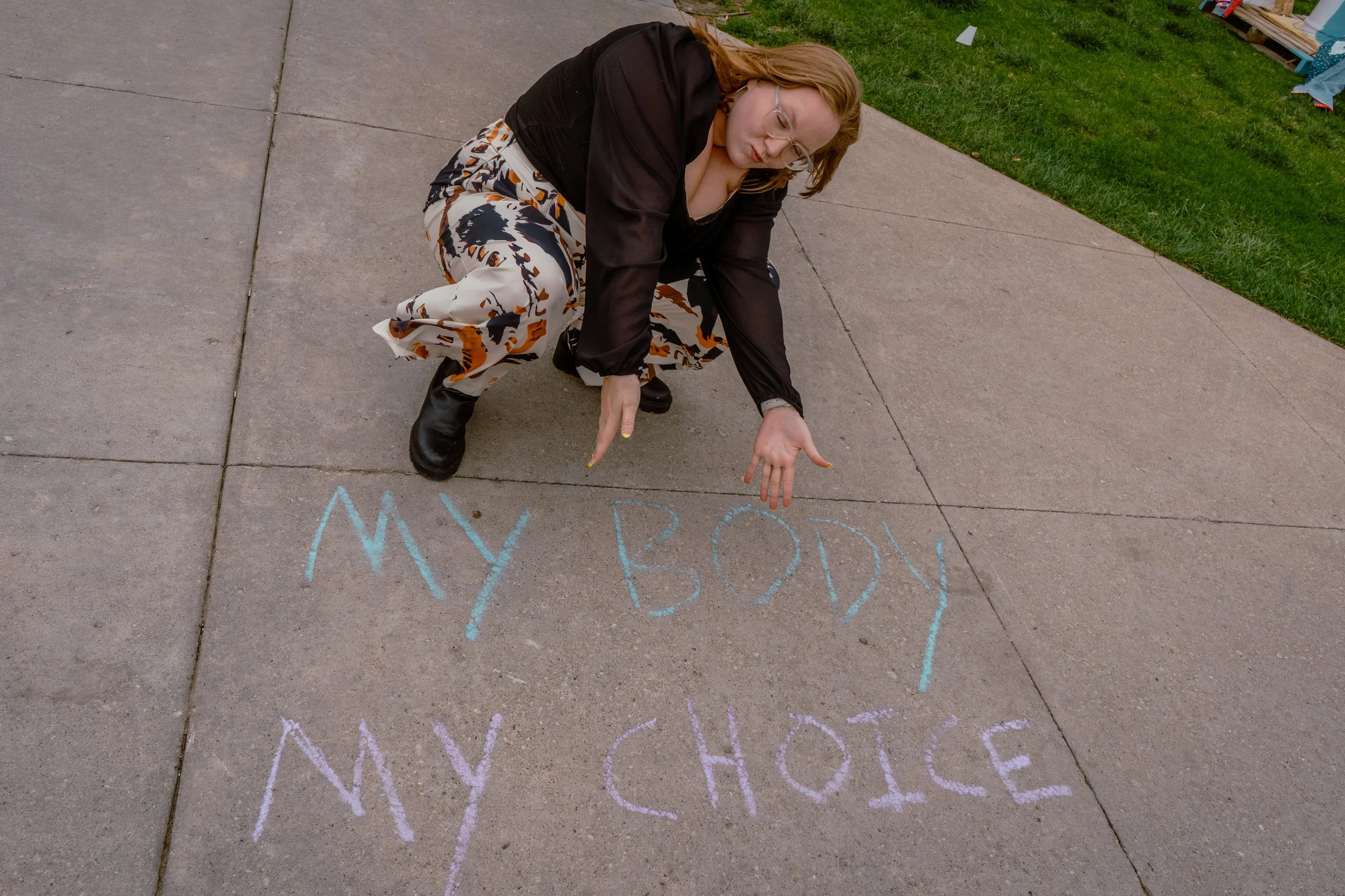 A WOMEN STANDING OUTSIDE OF THE UNIVERSITY IOWA OLD CAPITAL BUILDING FOR GRADUATION PHOTOS, NEXT TO SOME SIDWALK CHALK THAT SAYS, "MY BODY MY CHOICE"