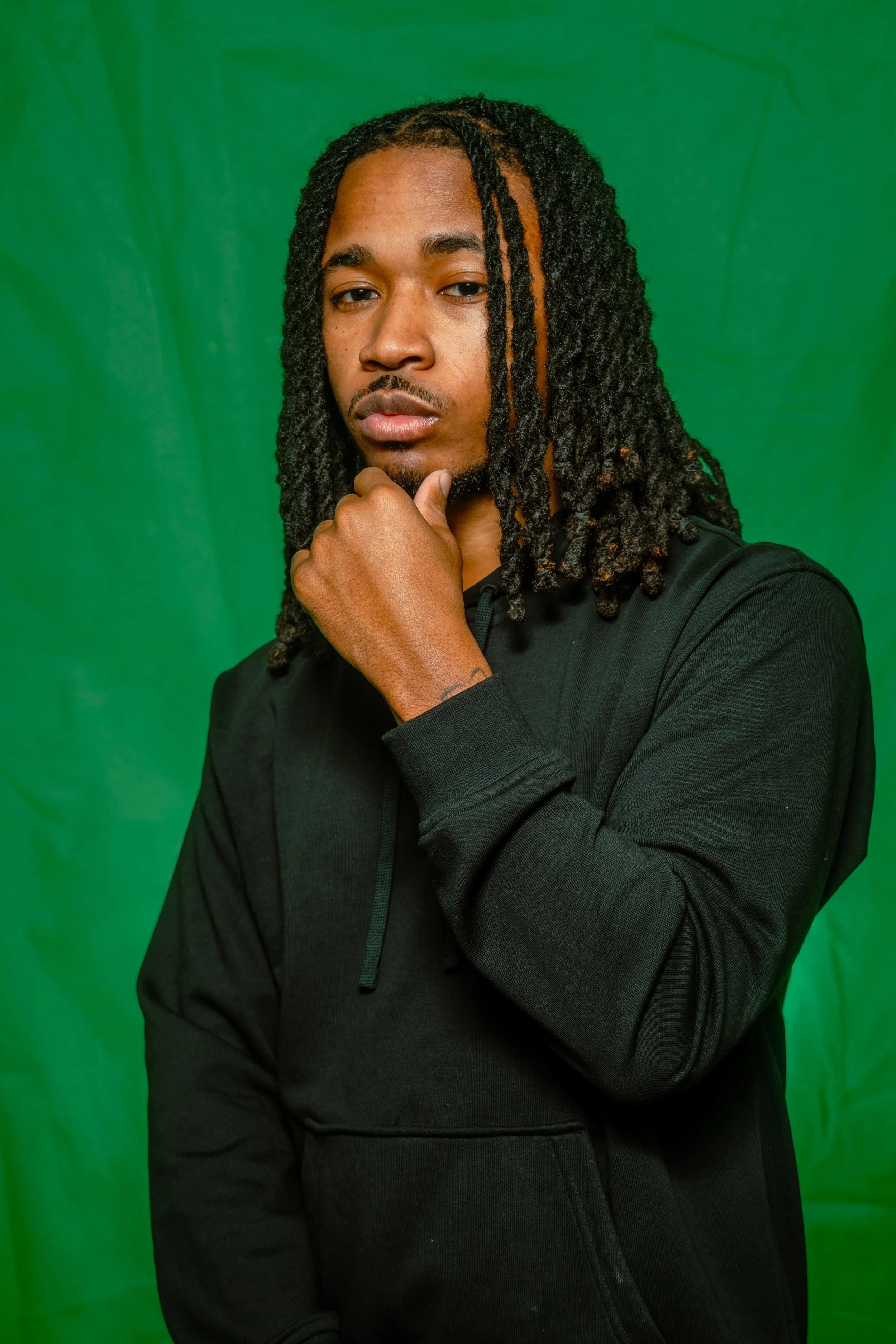 A PICTURE FROM A PHOTO STUDIO, A MAN IN FRONT OF A GREEN BACKGROUND, FIXING HIS HAIN WHILE HE LOOK AT THE CAMERA 